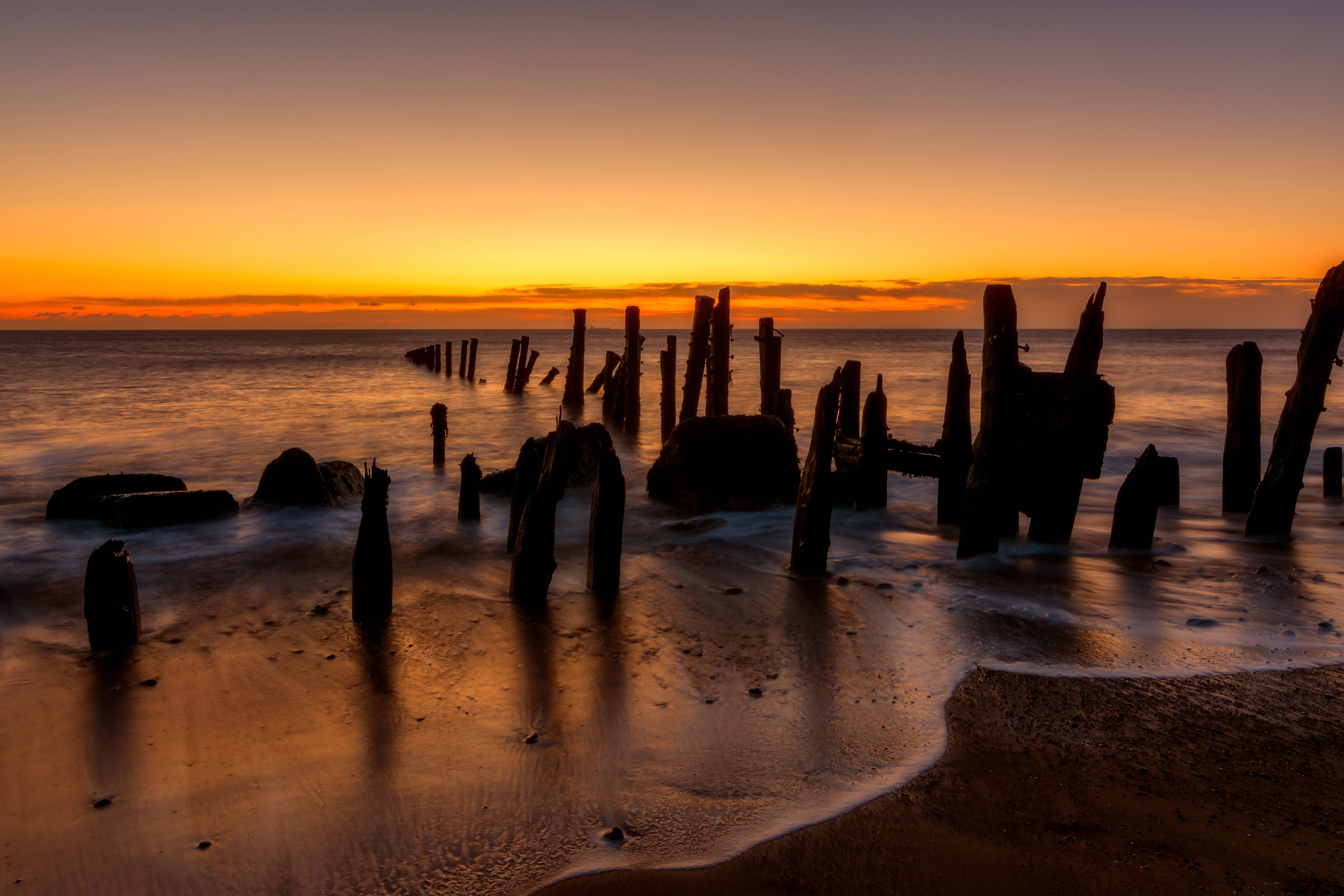 Wooden poles in the ocean at sunrise HD Wallpaper