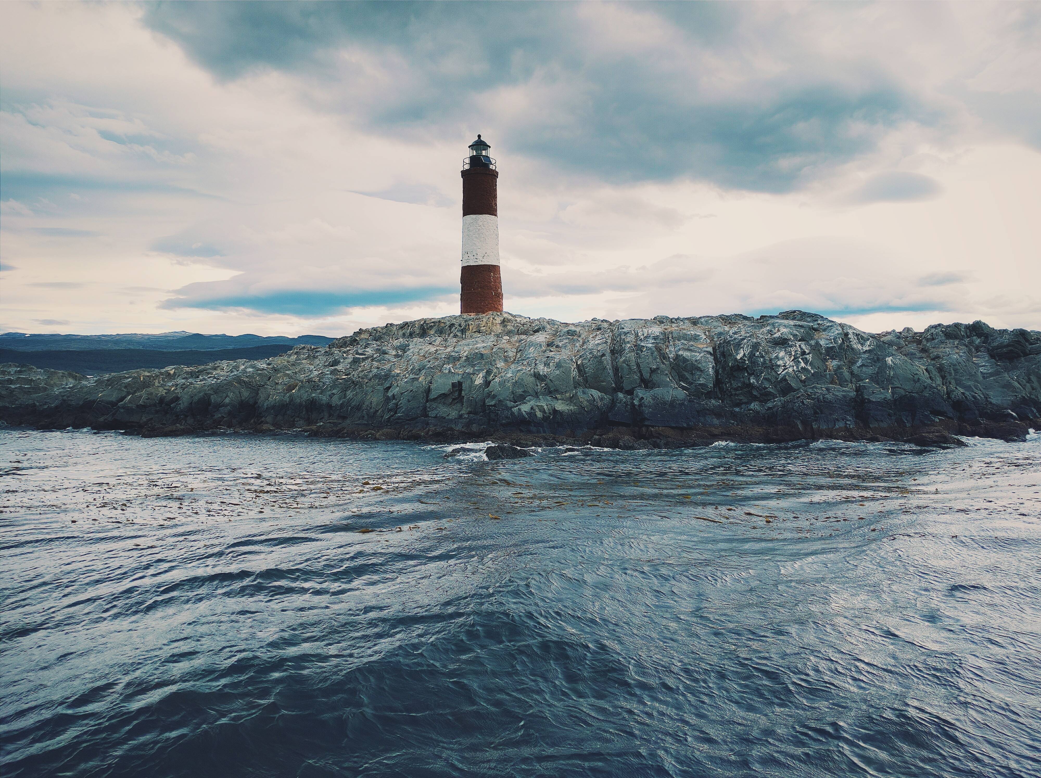 Lighthouse on a rocky island in the sea HD Wallpaper