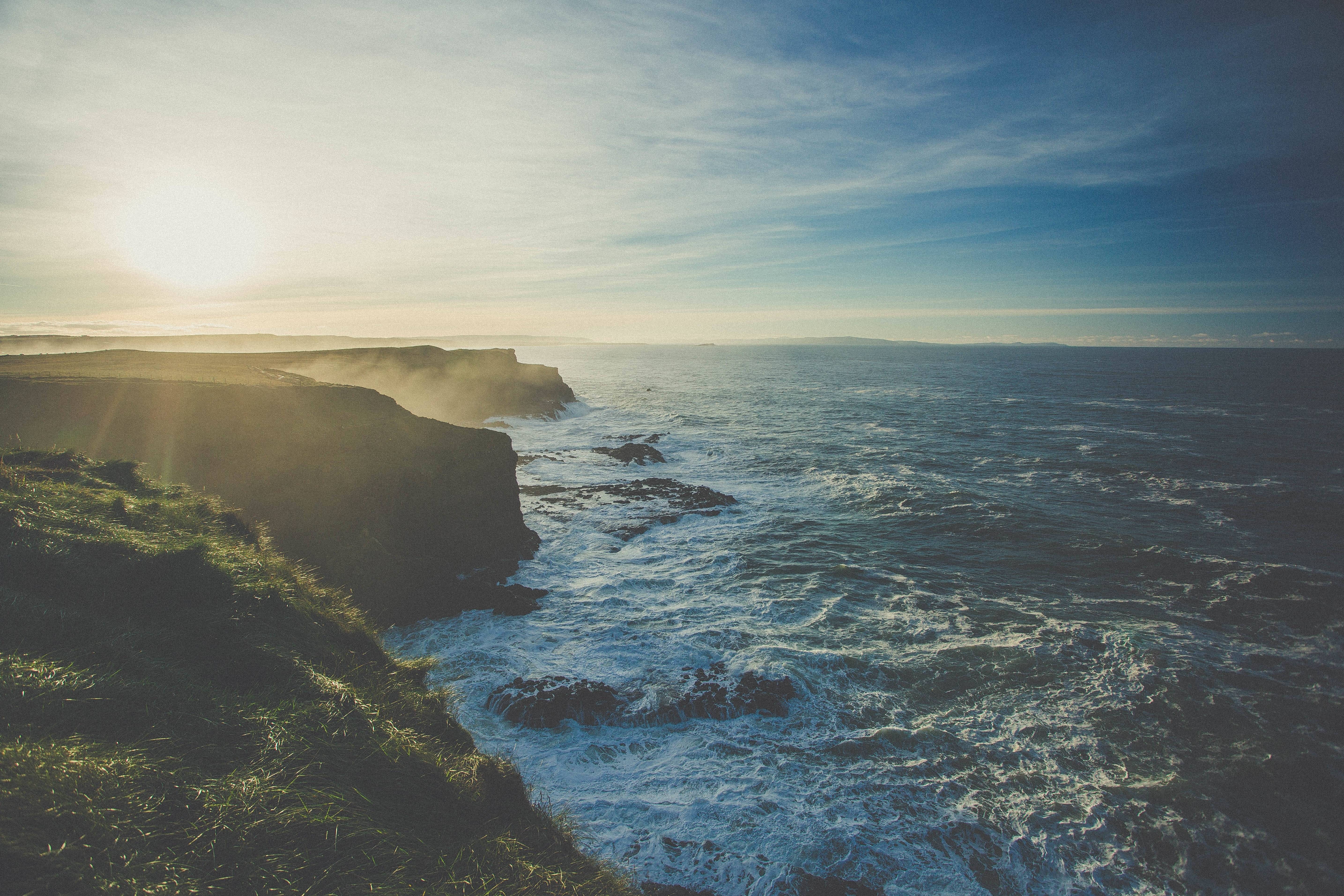 Rugged coastline with crashing waves under a bright sky HD Wallpaper