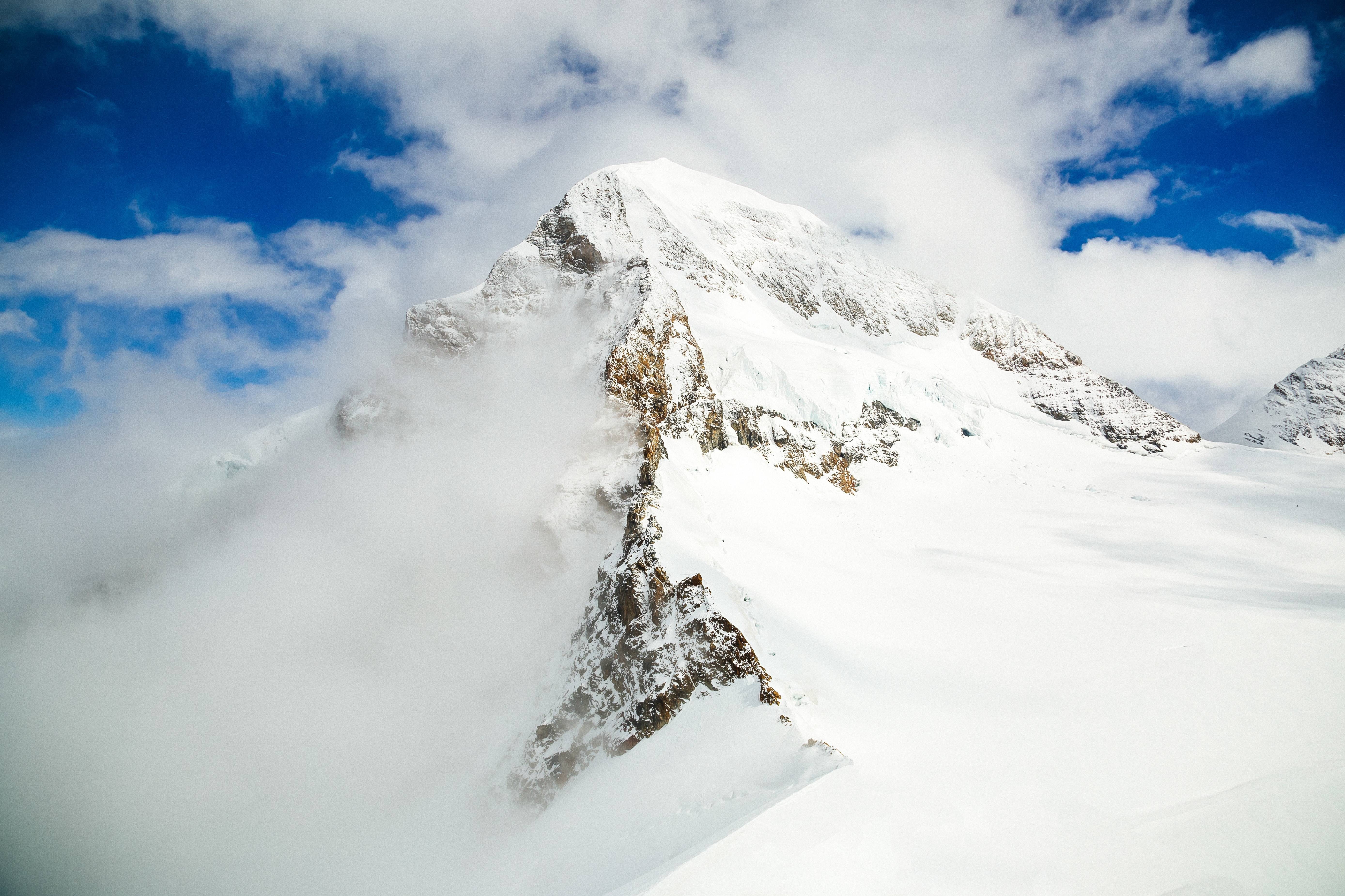 Snow-covered mountain peak shrouded in clouds HD Wallpaper
