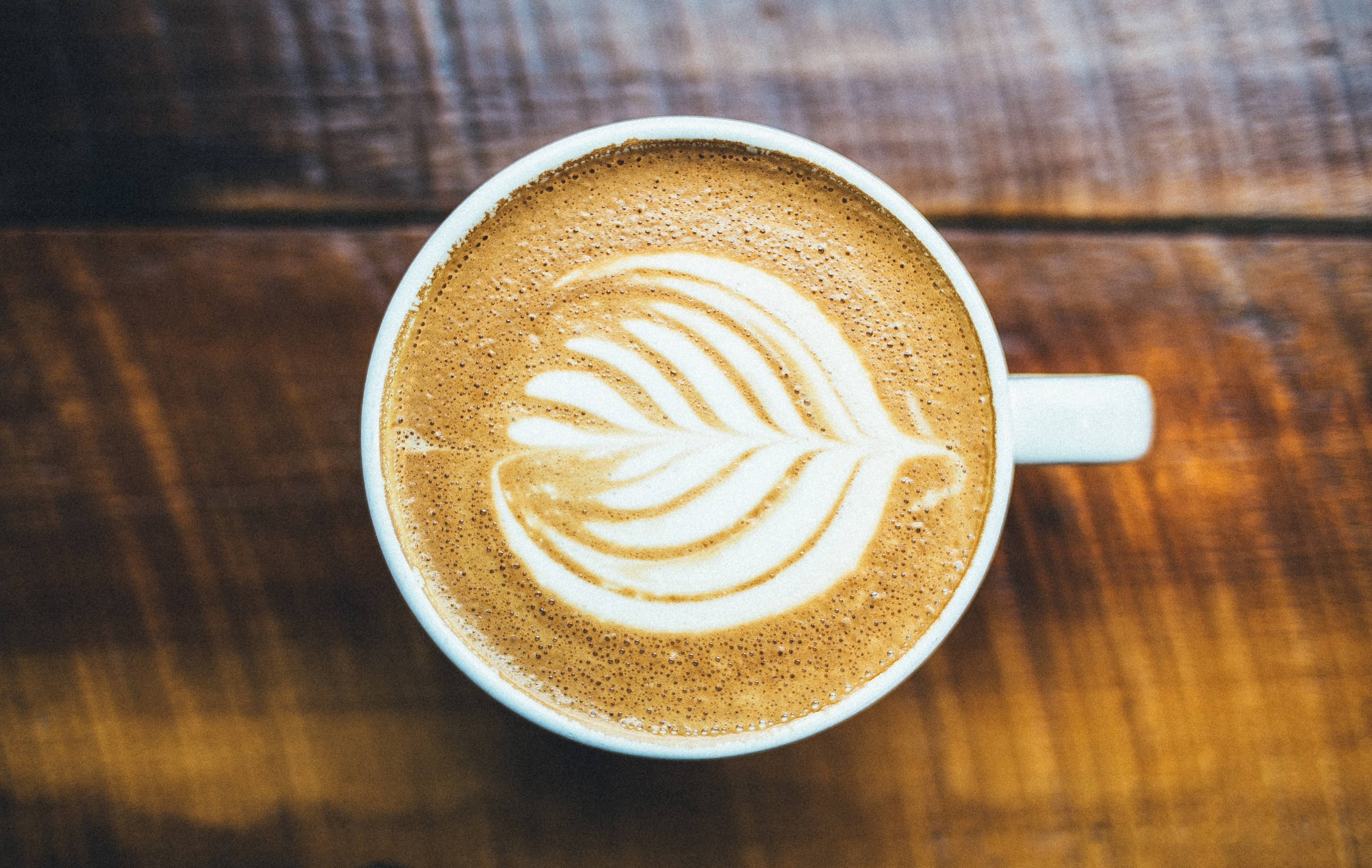 Latte art in a white mug on a wooden table HD Wallpaper