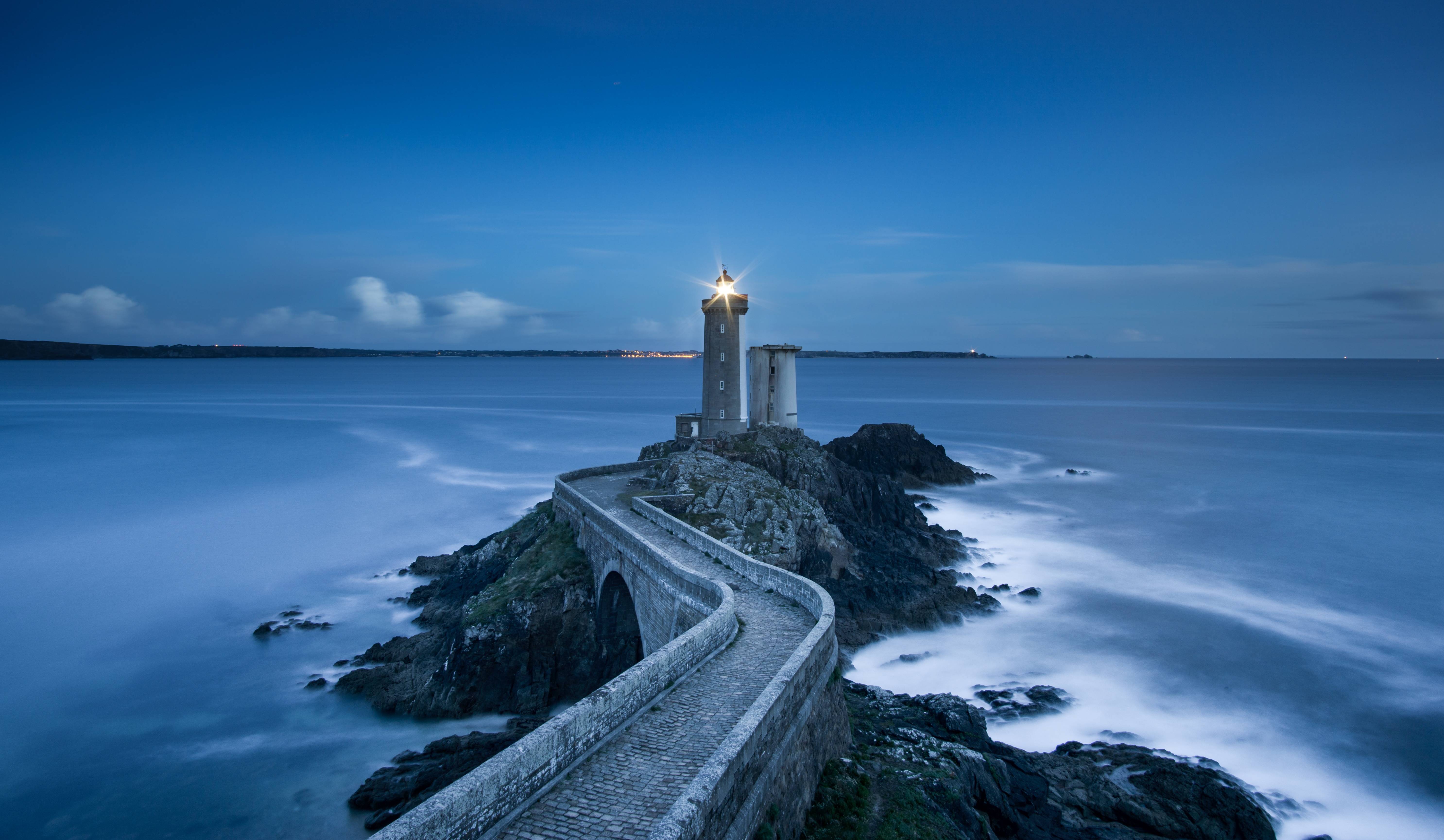 Lighthouse on a rocky island with a stone bridge HD Wallpaper