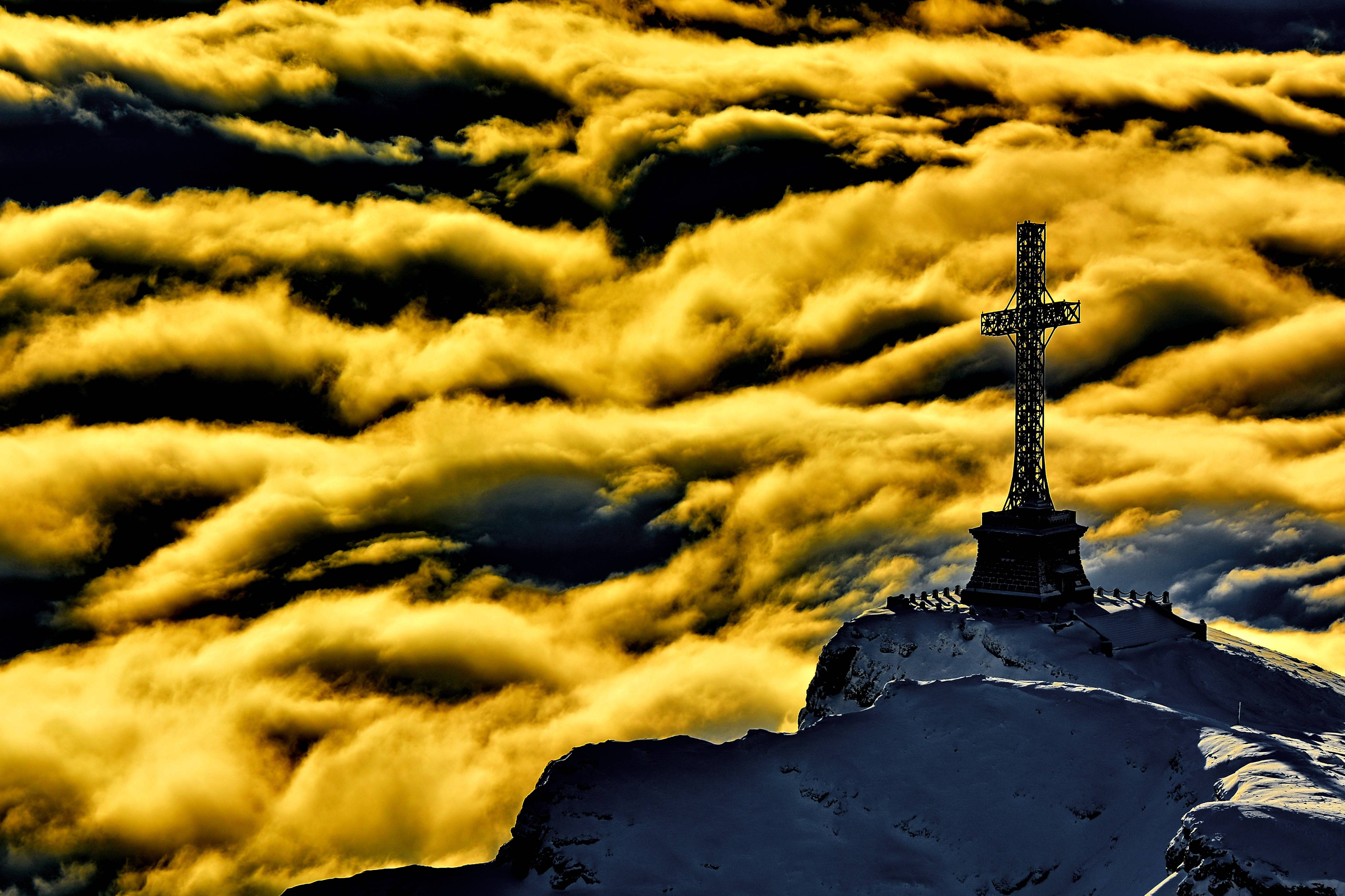 Cross on a snowy mountain peak above clouds HD Wallpaper