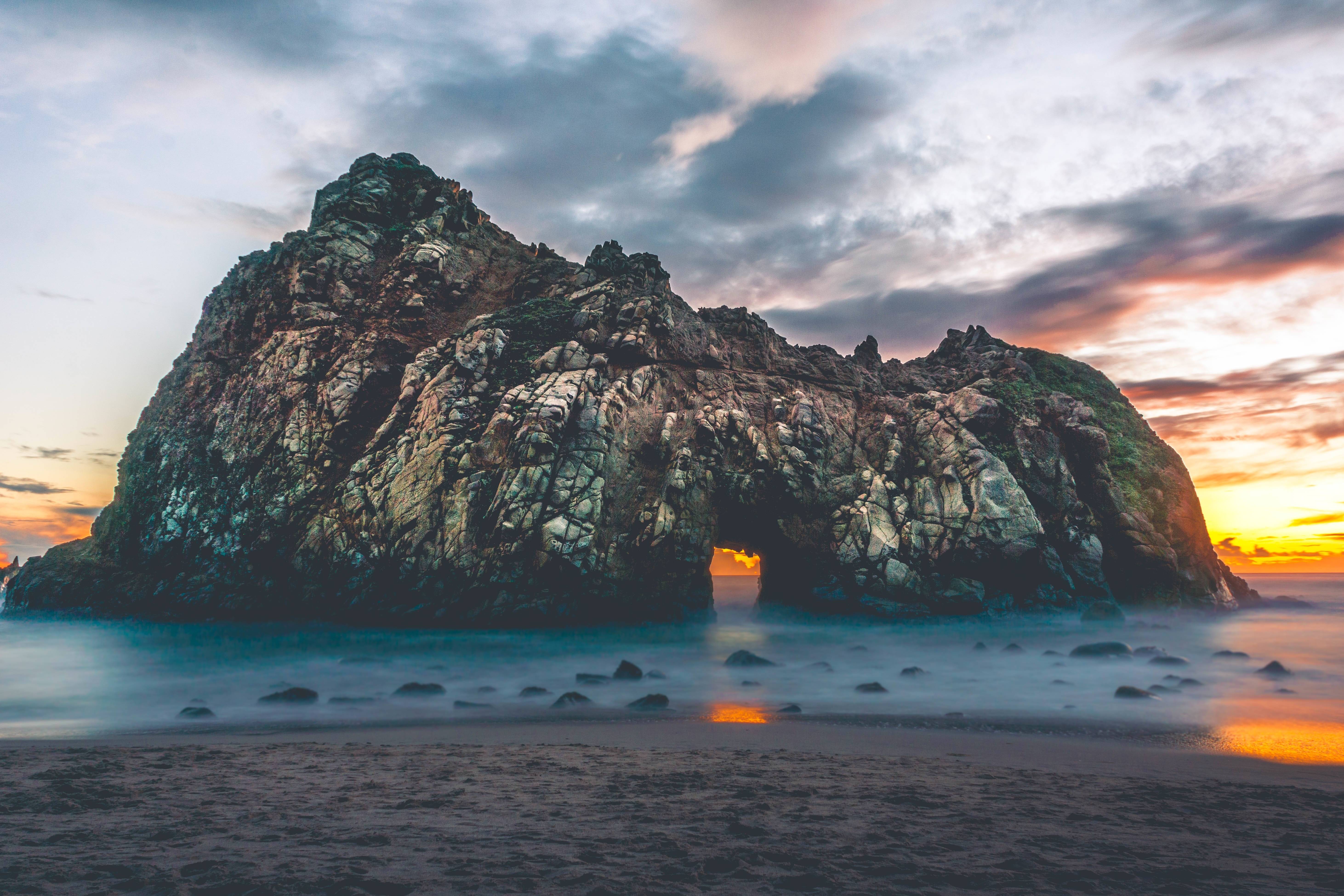 Rock formation with archway in the ocean at sunset HD Wallpaper