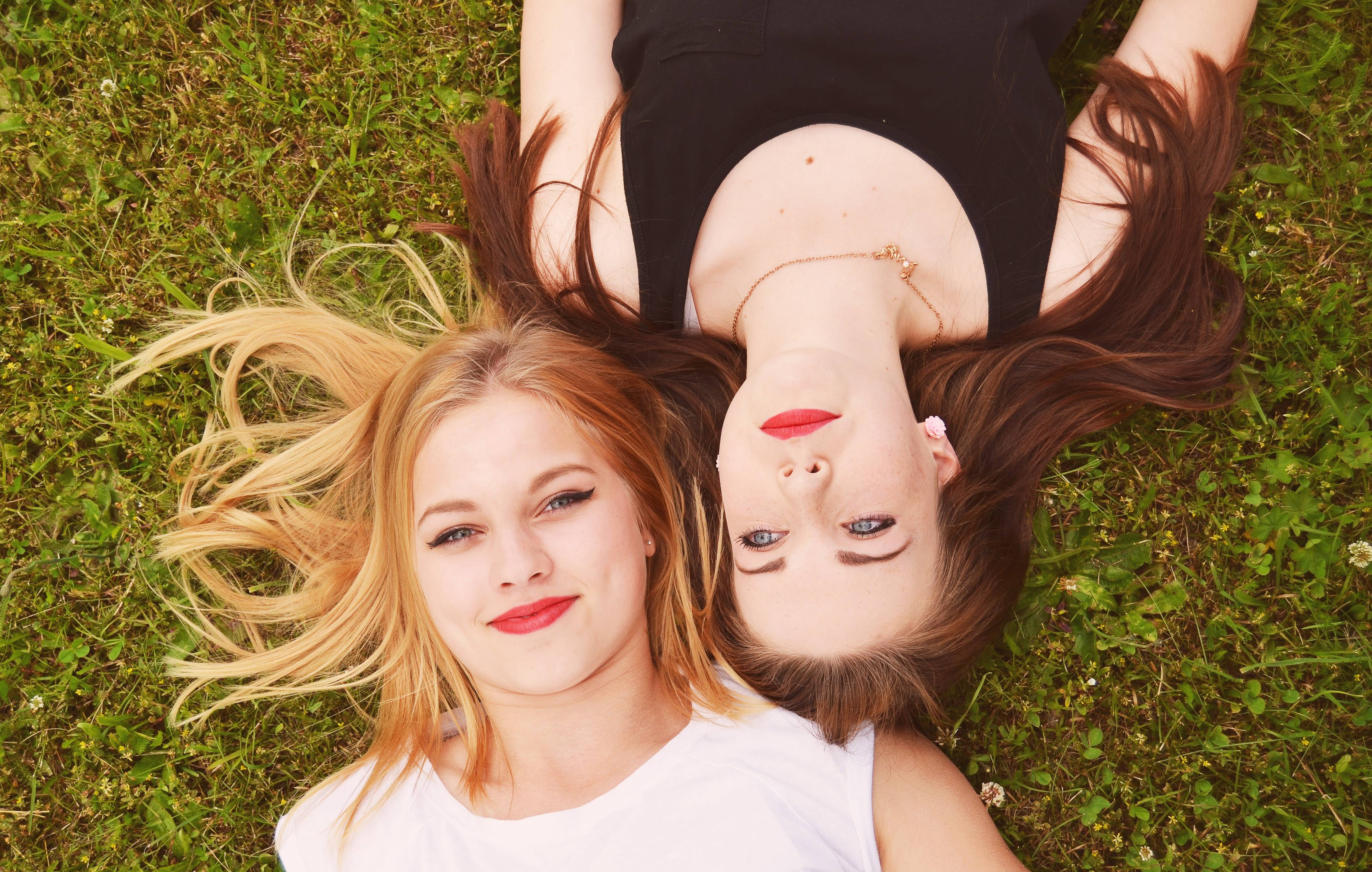 Two young women with blonde and brown hair lying on grass HD Wallpaper