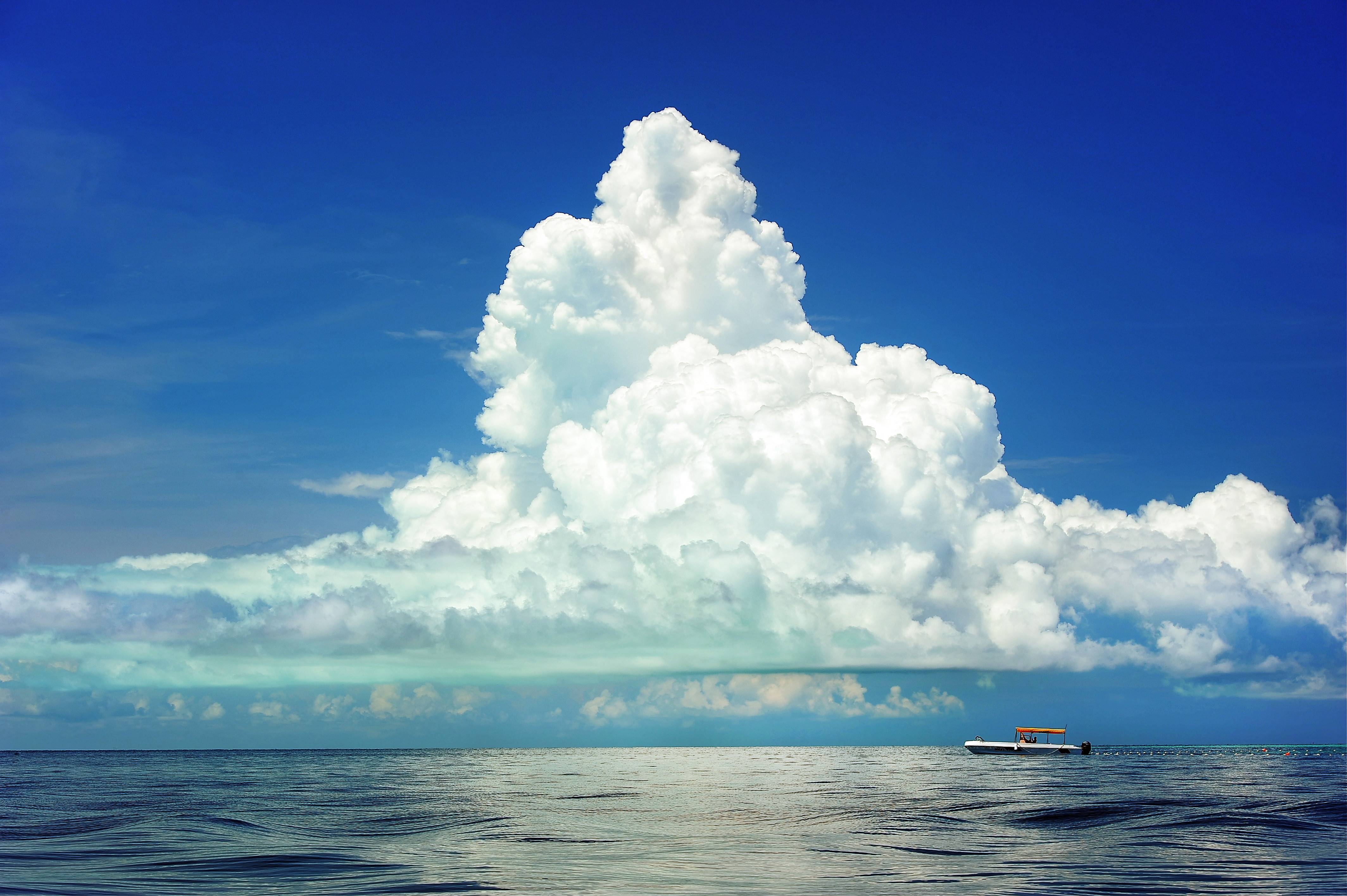 A boat on the ocean under a large cumulus cloud HD Wallpaper