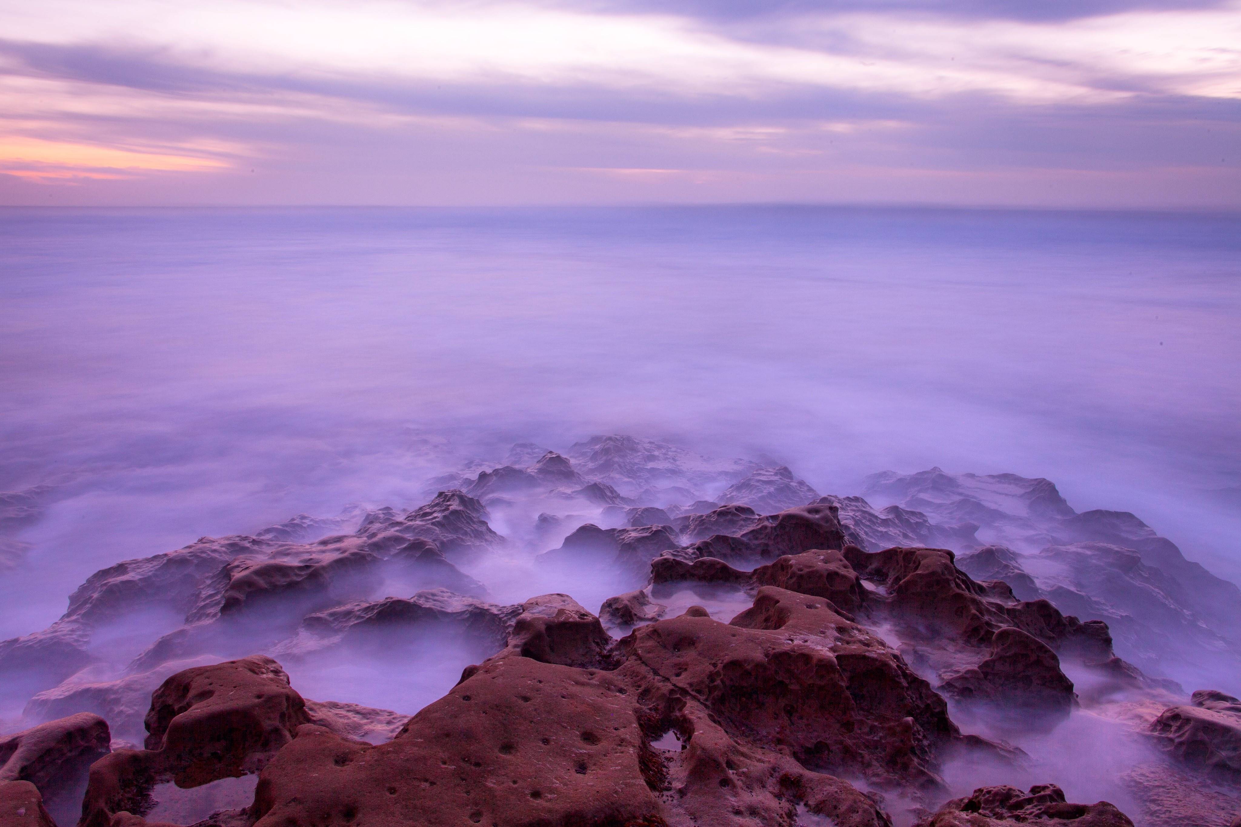 Rocky coast at dusk with purple clouds and ocean HD Wallpaper