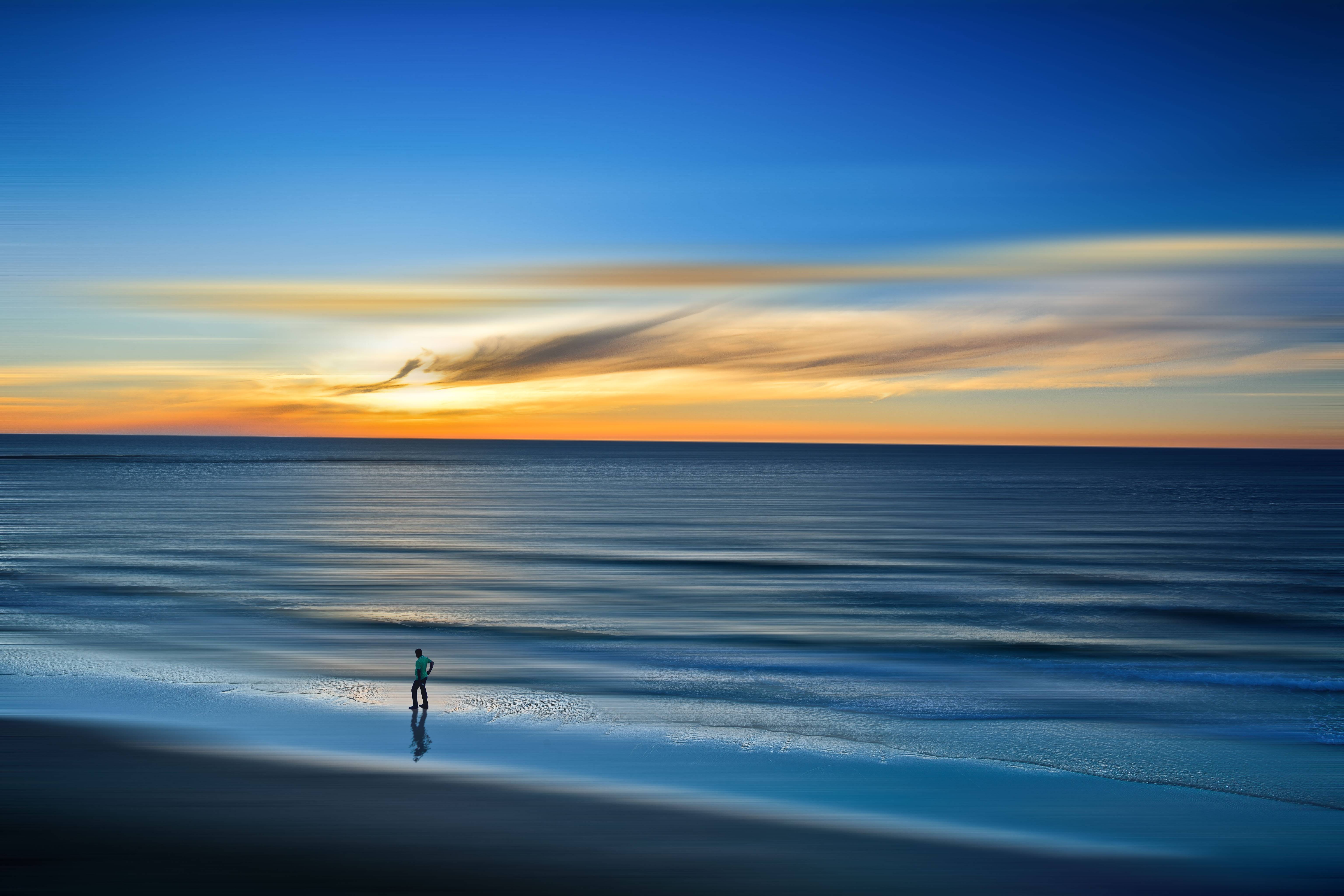 Man walking on a beach at sunset HD Wallpaper