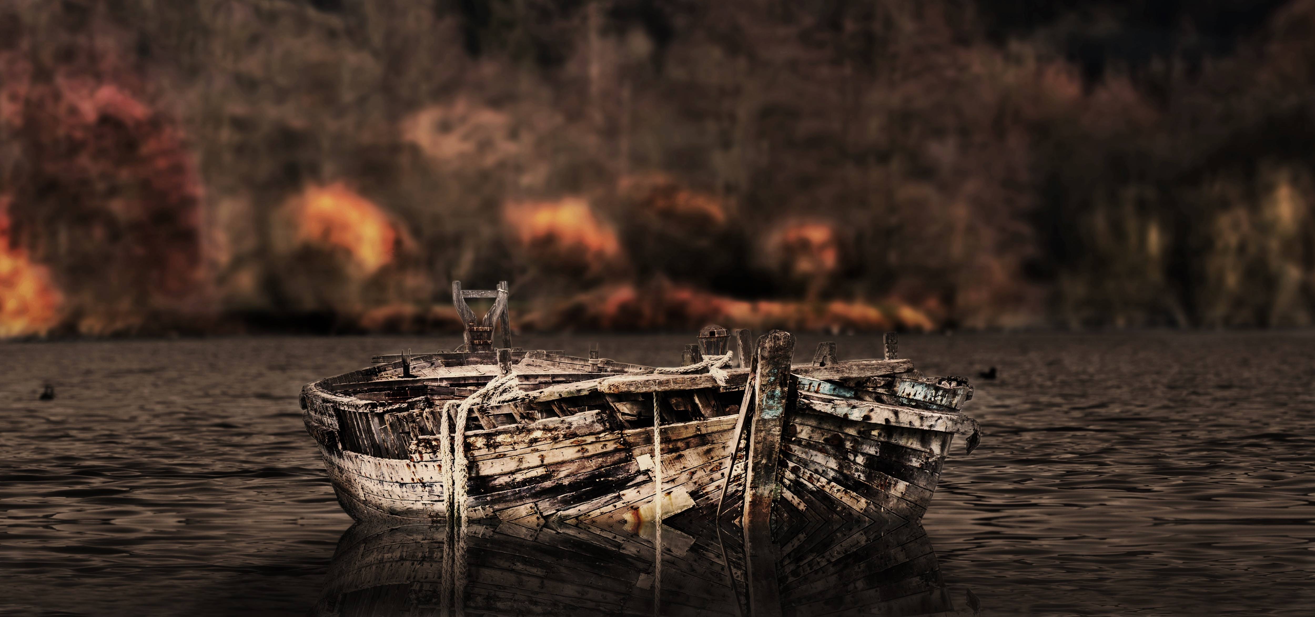 Old wooden boat on the water with fire in the background HD Wallpaper
