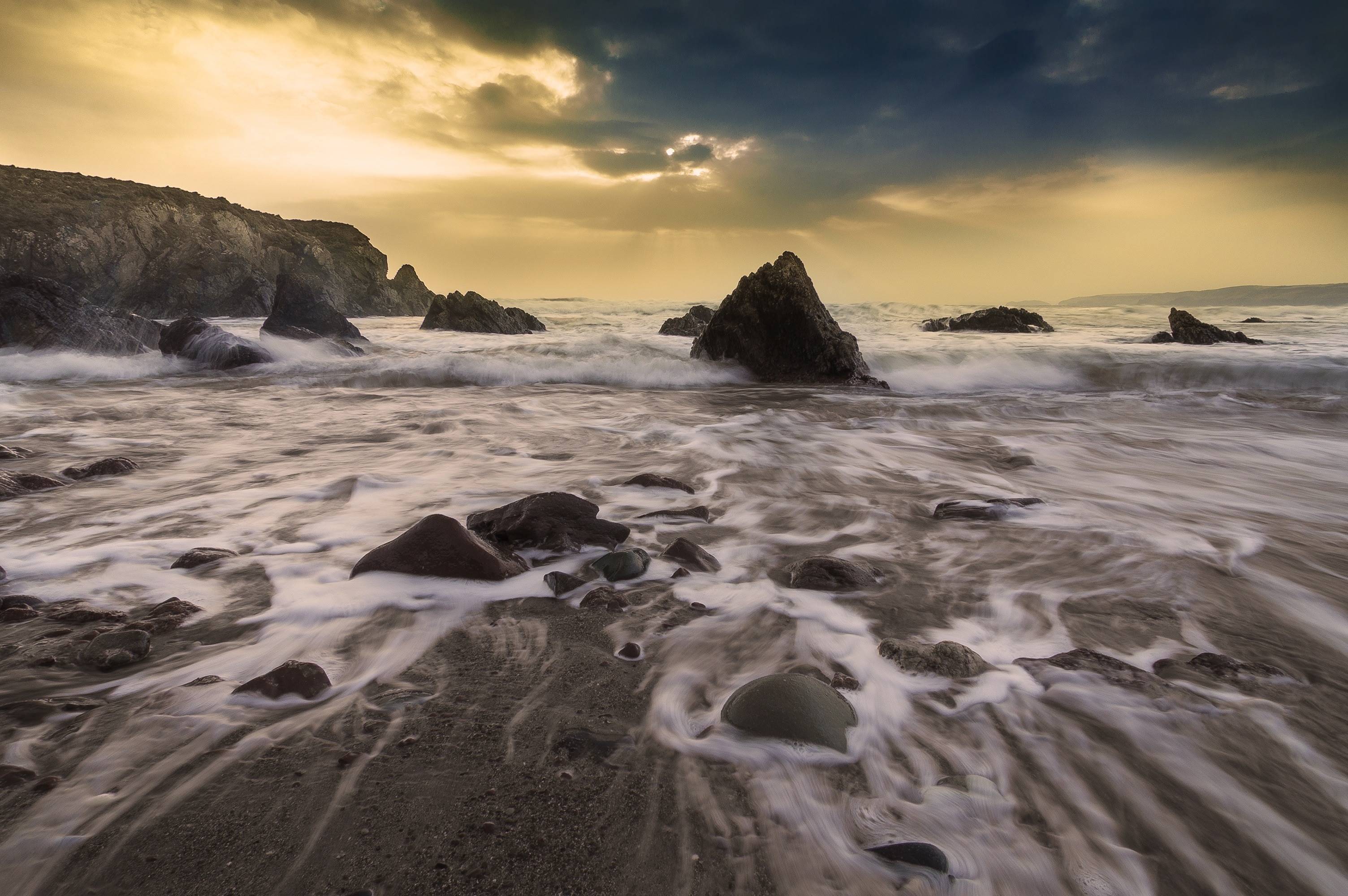 Waves crashing on a rocky shore under a dramatic sky HD Wallpaper