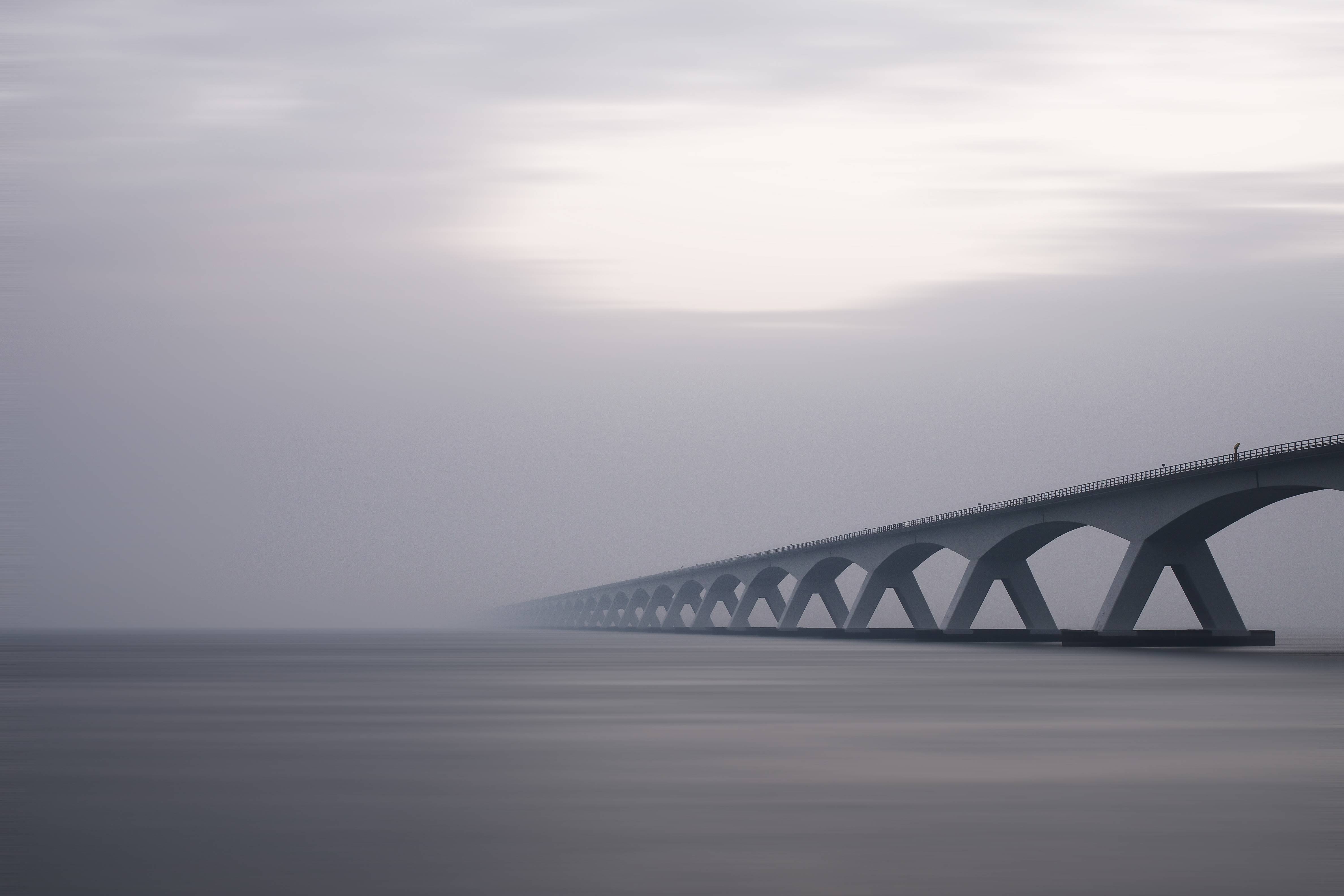 Long concrete bridge with arches over water HD Wallpaper