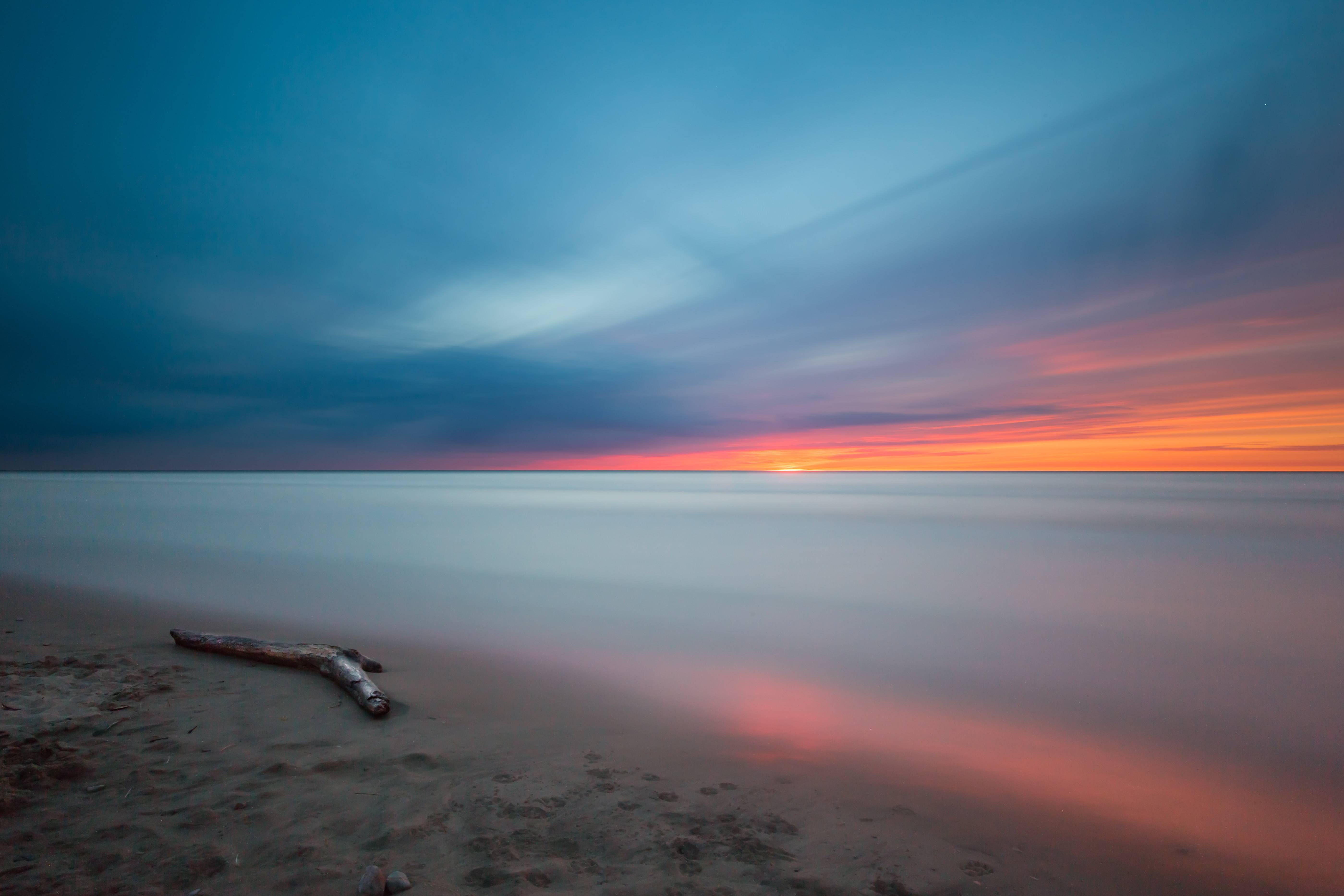 Sunset over the ocean with driftwood on the beach HD Wallpaper