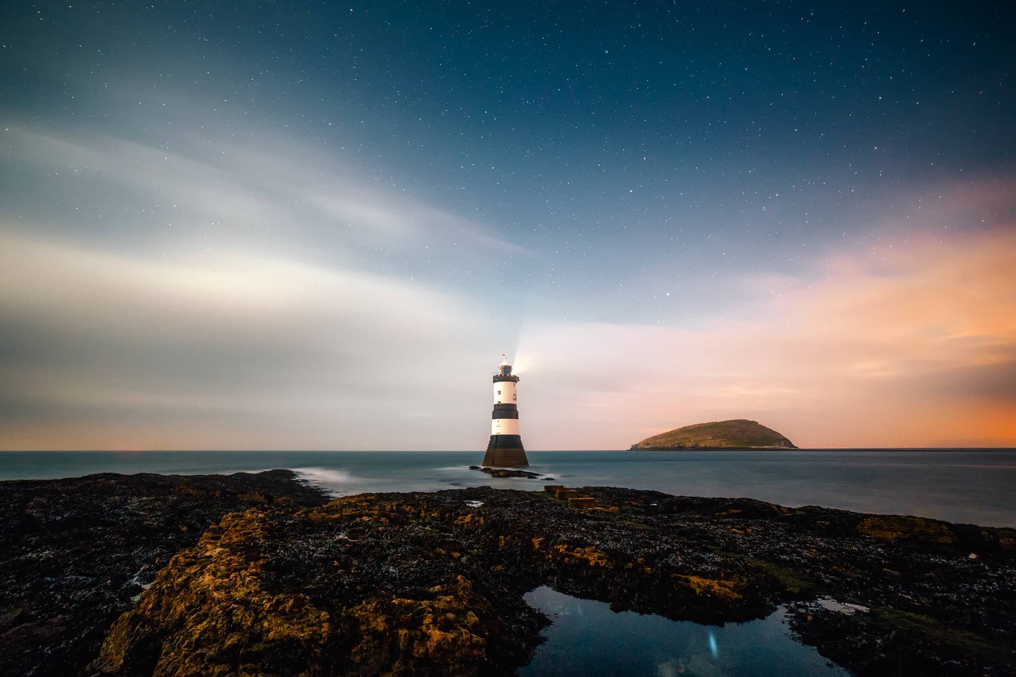 Lighthouse on a rocky shore under a starry sky HD Wallpaper
