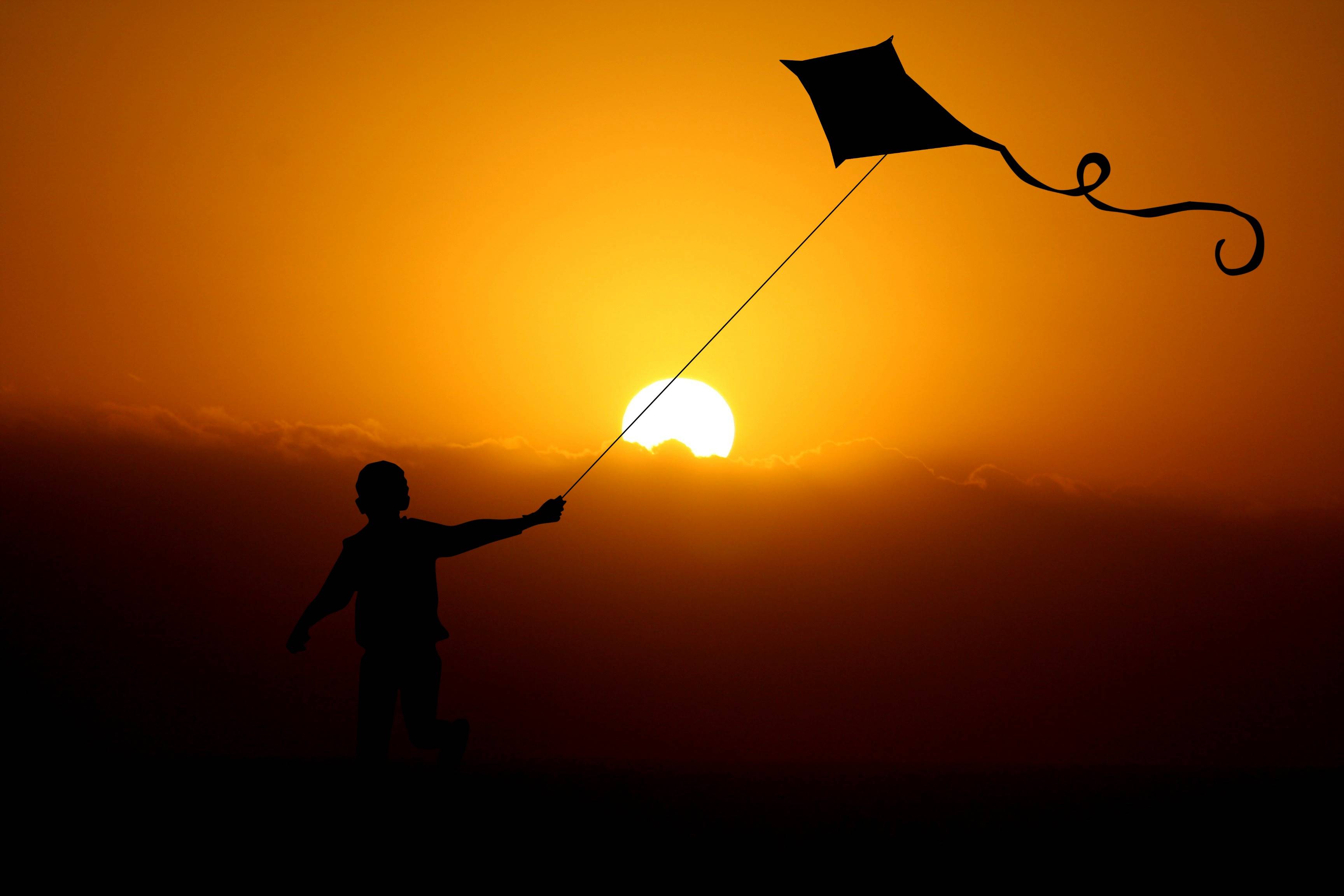 Silhouette of a boy flying a kite at sunset HD Wallpaper