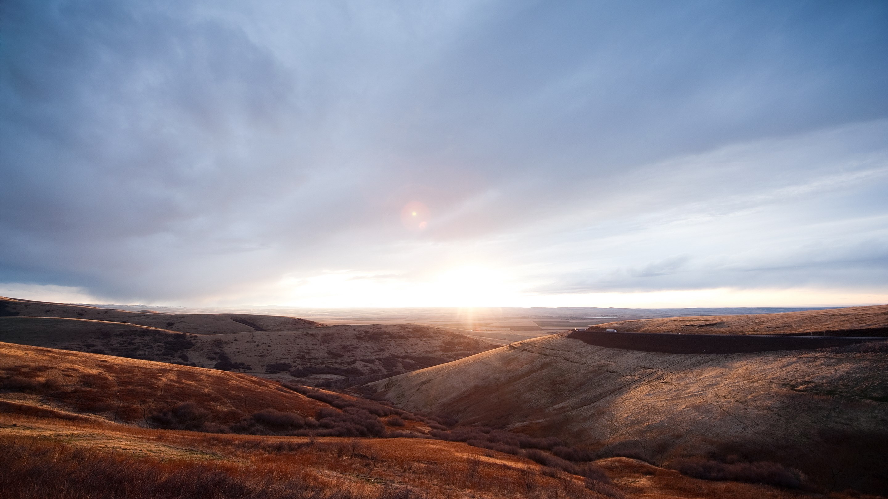 Sunset over rolling hills with a road HD Wallpaper