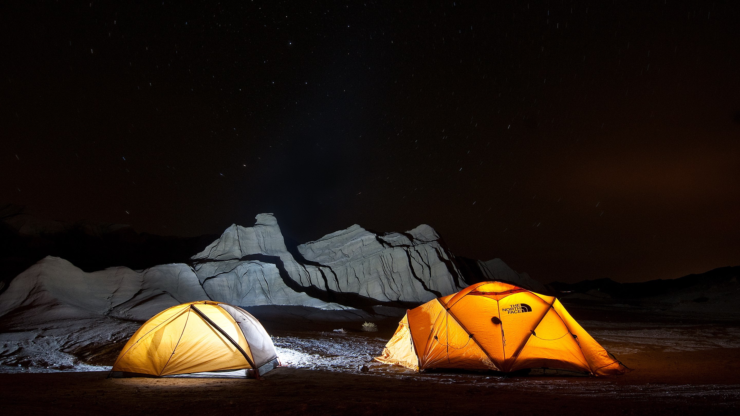 Two illuminated tents under a starry night sky HD Wallpaper