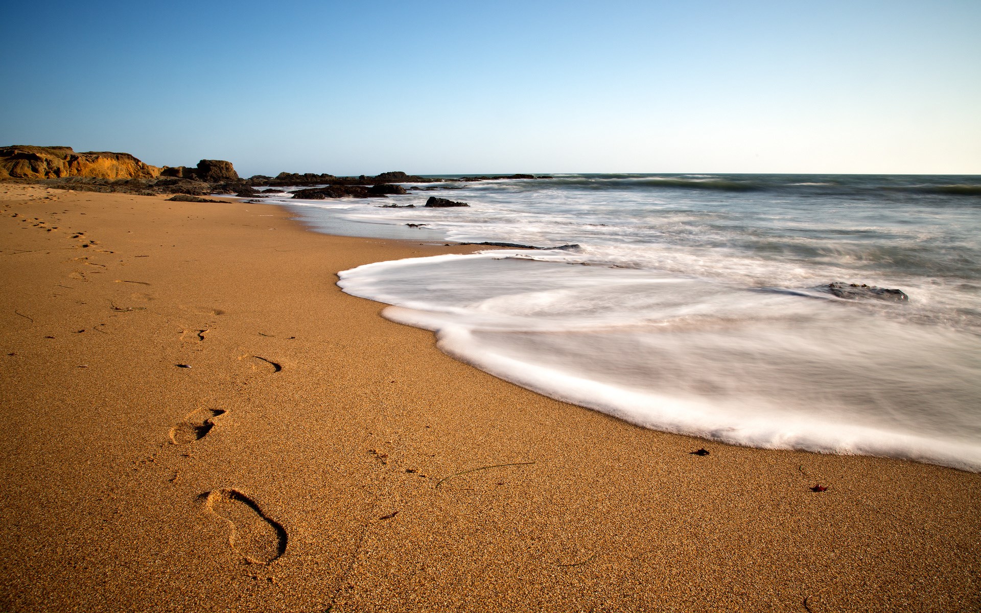 Footprints on a sandy beach with ocean waves HD Wallpaper