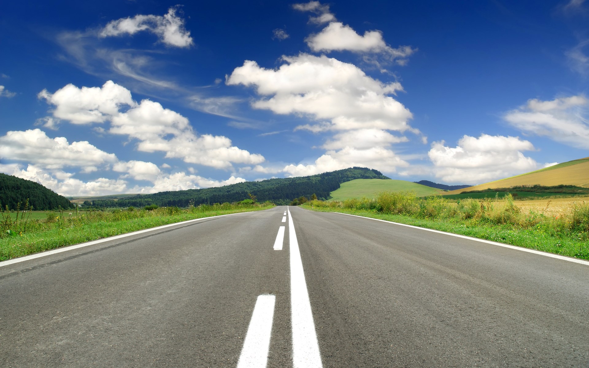 Empty road through rolling hills under a blue sky HD Wallpaper