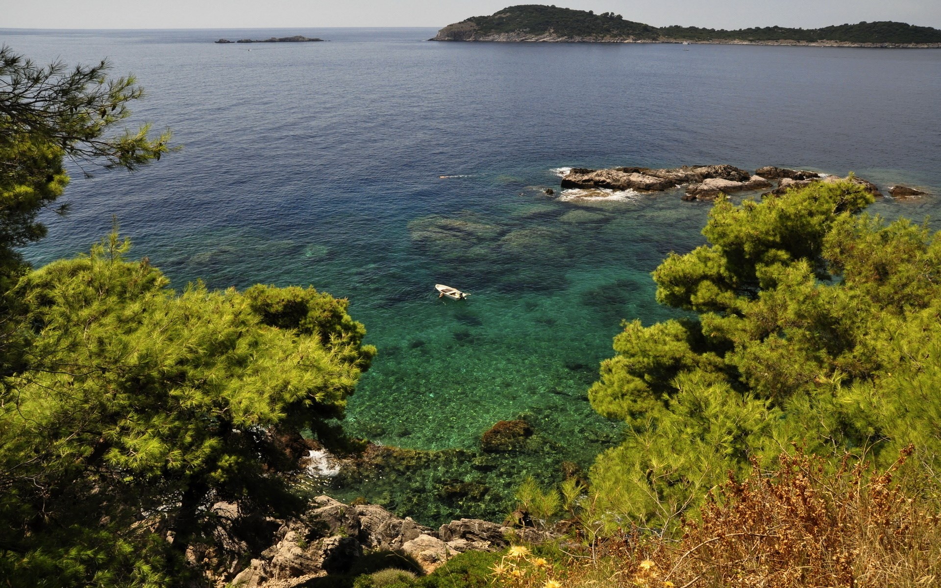 Boat in clear turquoise water near rocky coast HD Wallpaper