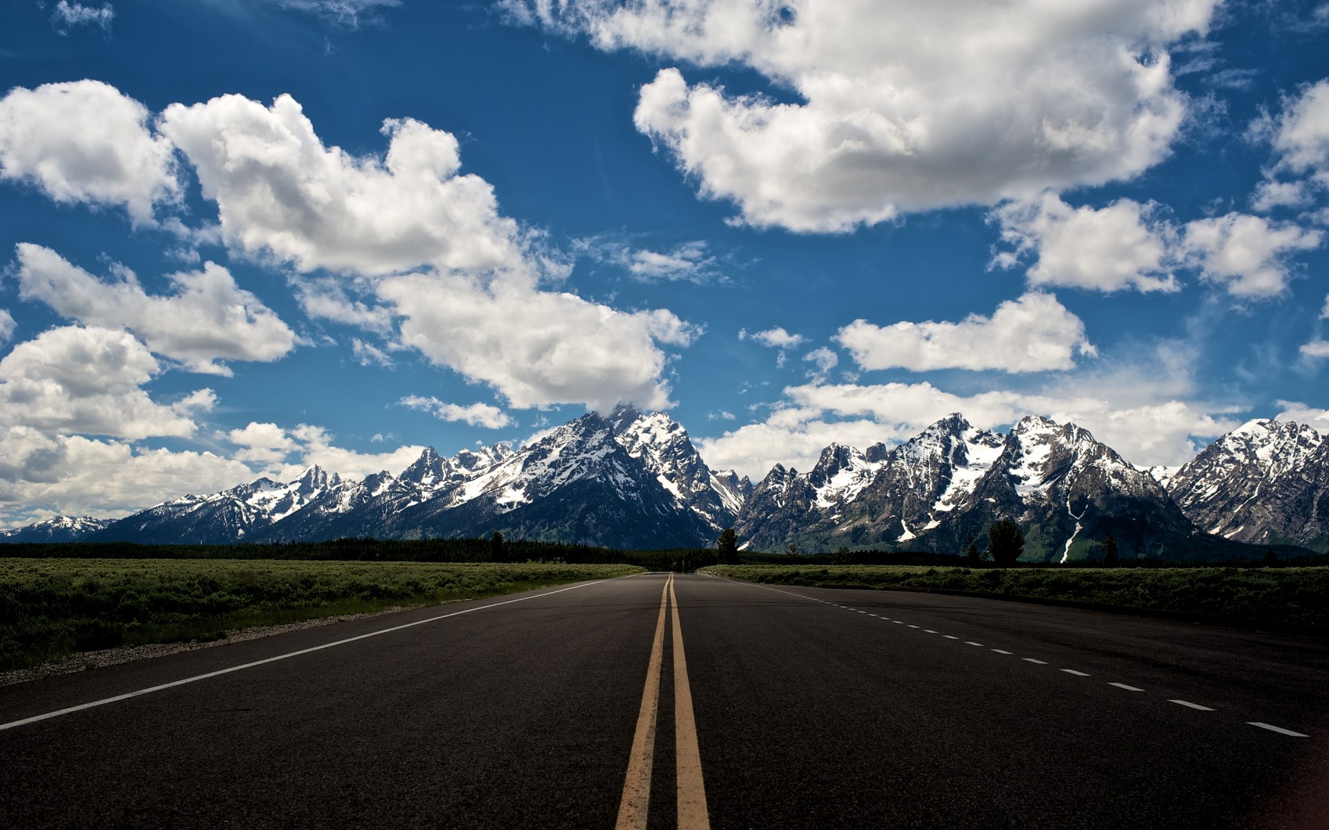 Road leading to snow-capped mountains under a cloudy sky HD Wallpaper
