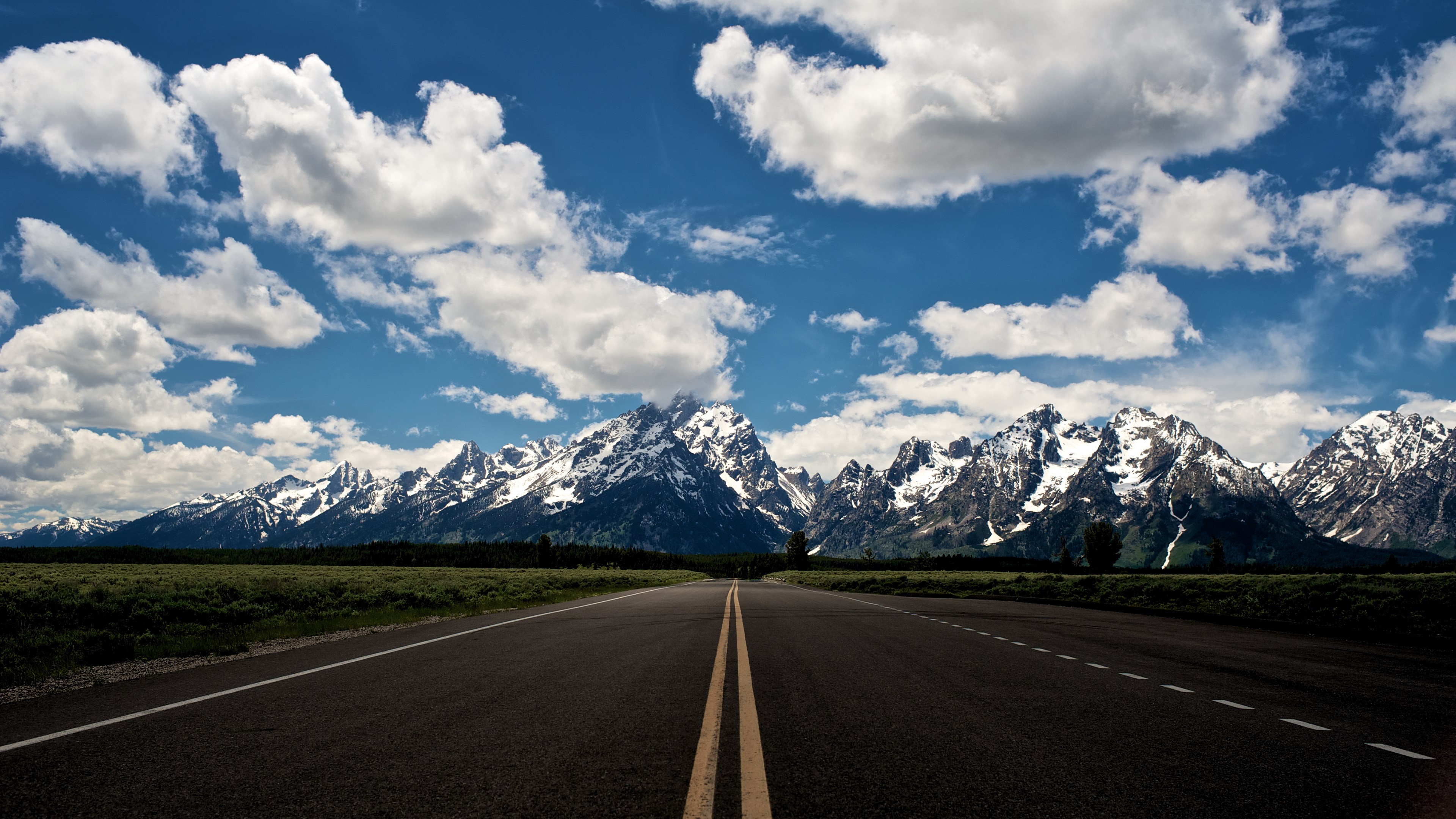 Road leading to snow-capped mountains under a cloudy sky HD Wallpaper