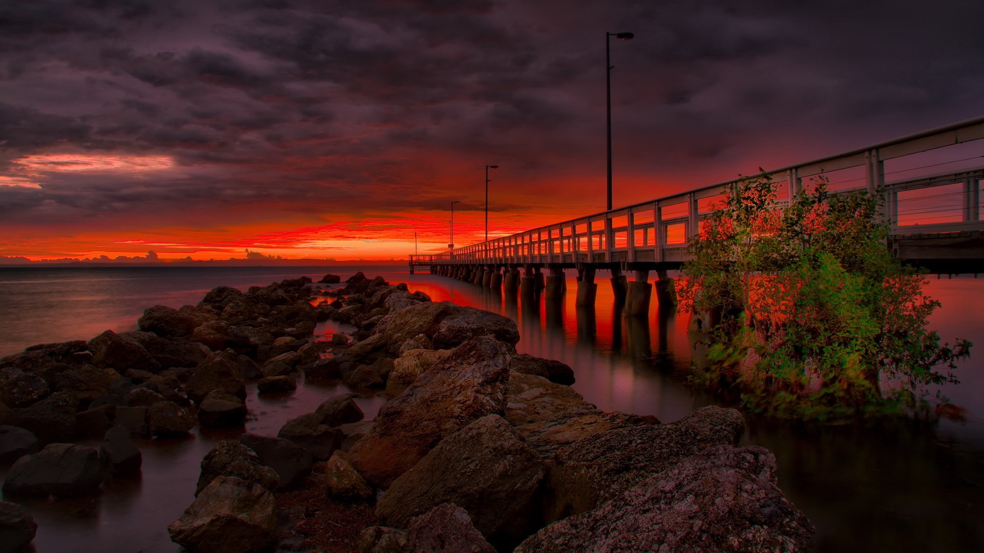 Pier over water at sunset with rocks HD Wallpaper