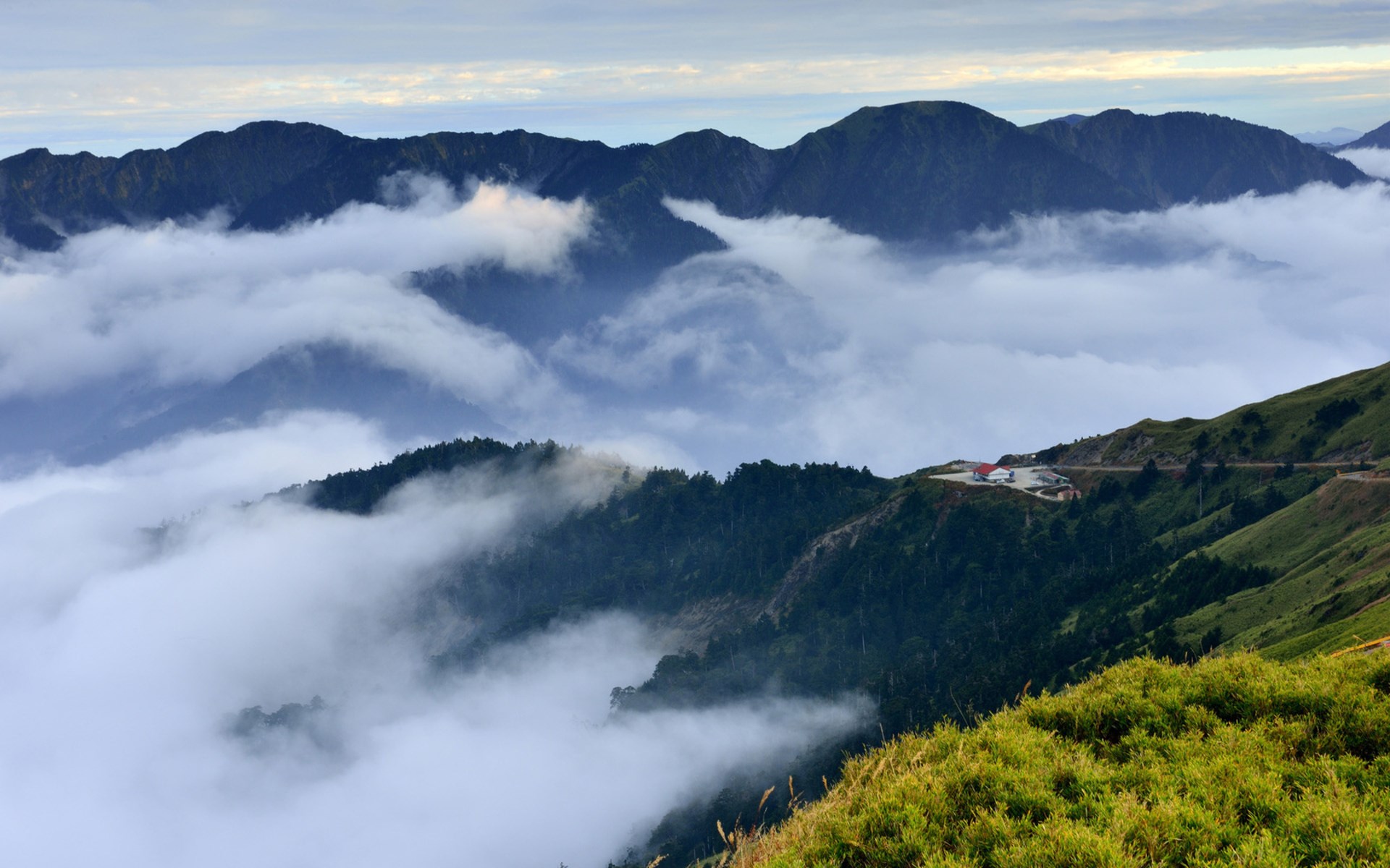 Mountains shrouded in clouds with a road and buildings HD Wallpaper