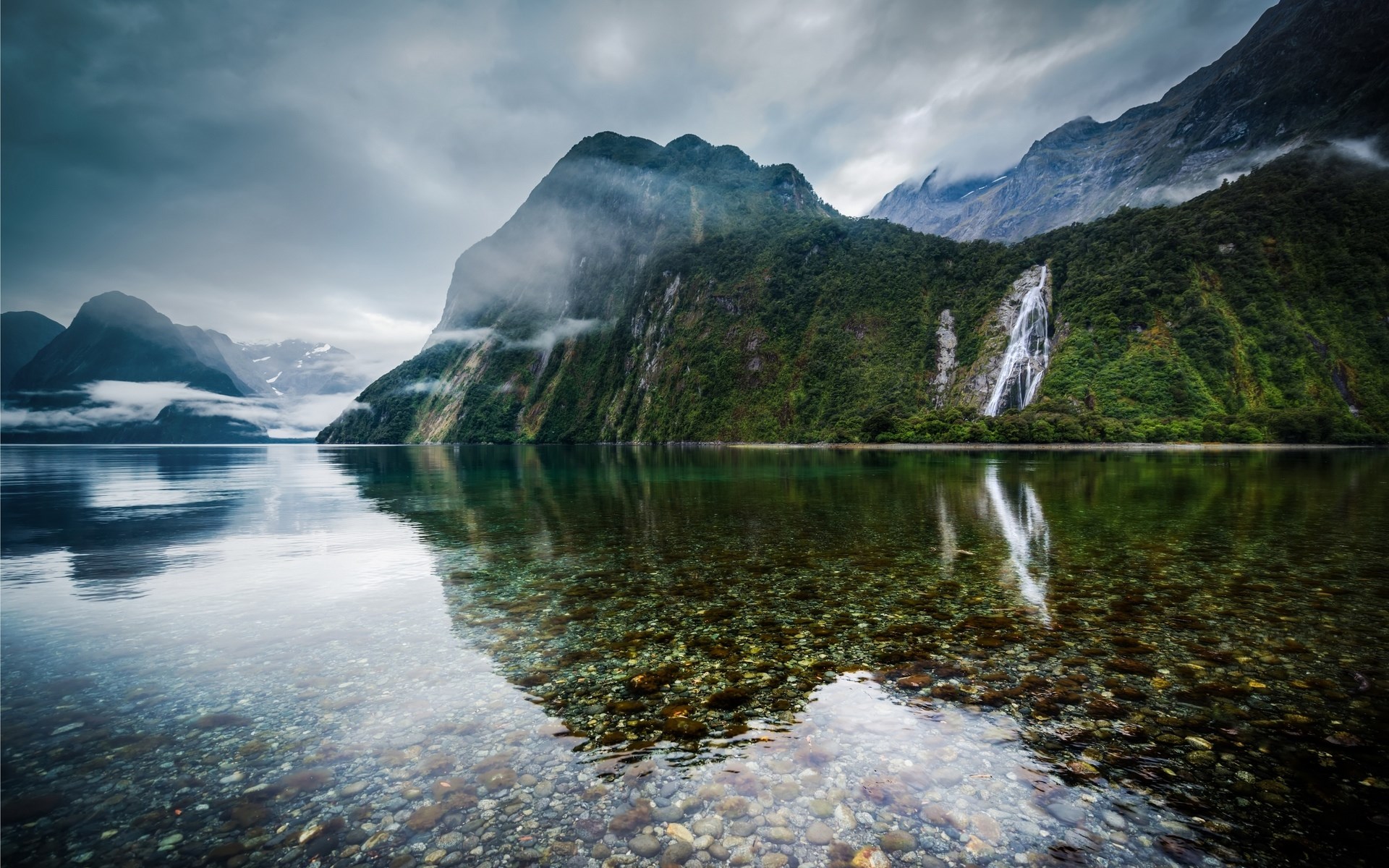 Waterfall cascading down a misty mountain into a calm lake HD Wallpaper