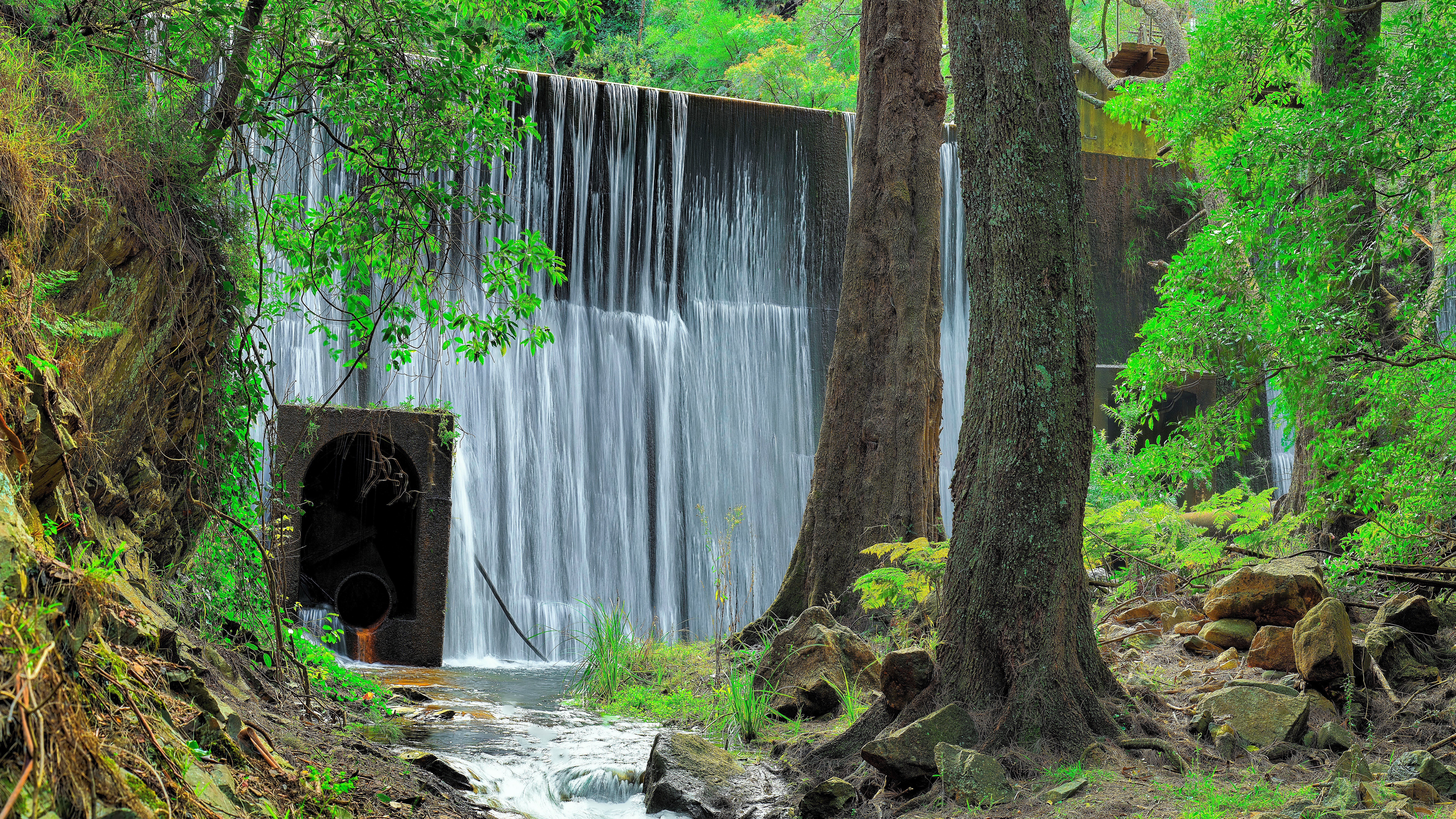 Waterfall cascading over a concrete dam with trees HD Wallpaper