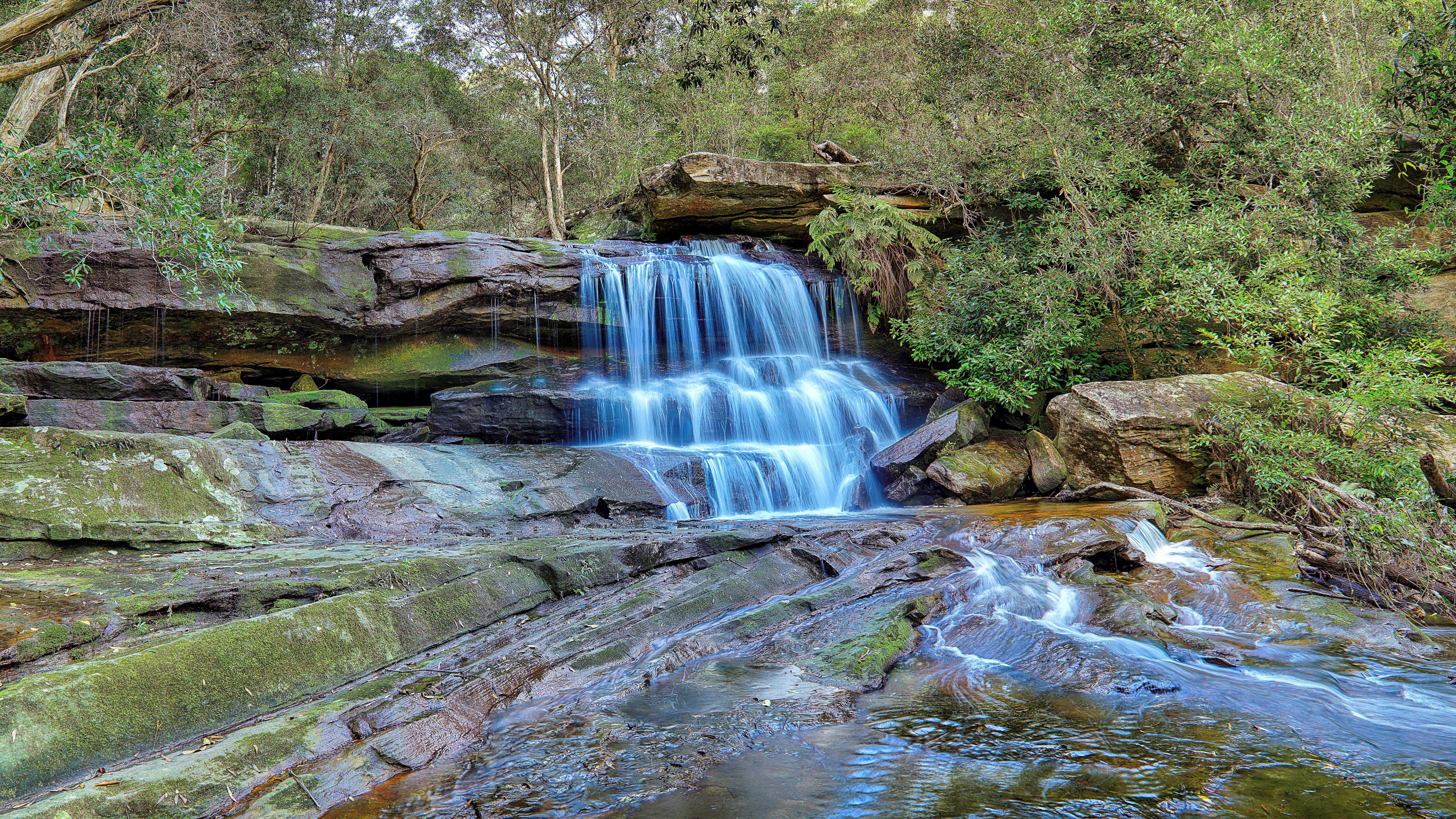 Waterfall cascading over mossy rocks in a forest HD Wallpaper