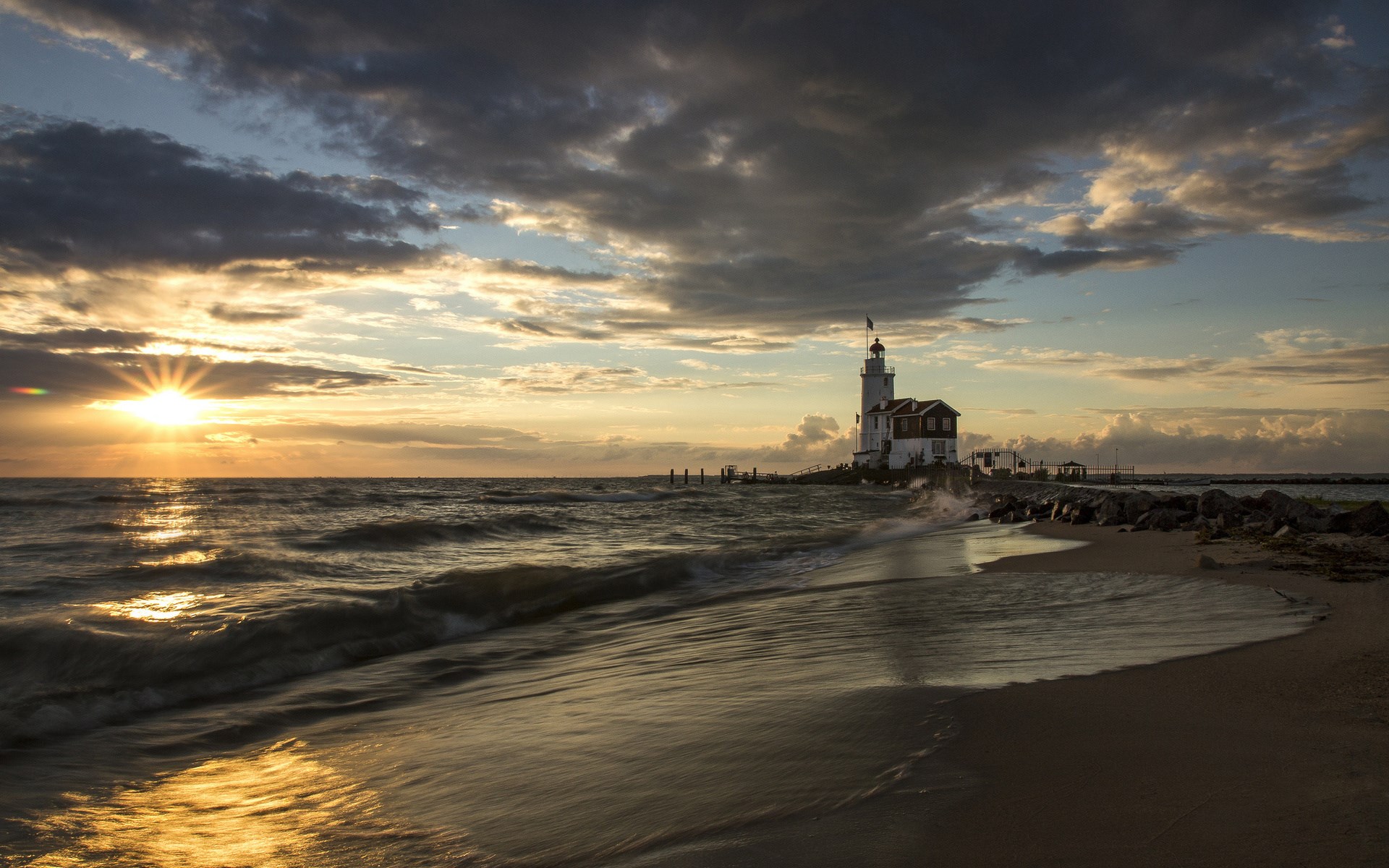 Lighthouse on a rocky shore at sunset HD Wallpaper