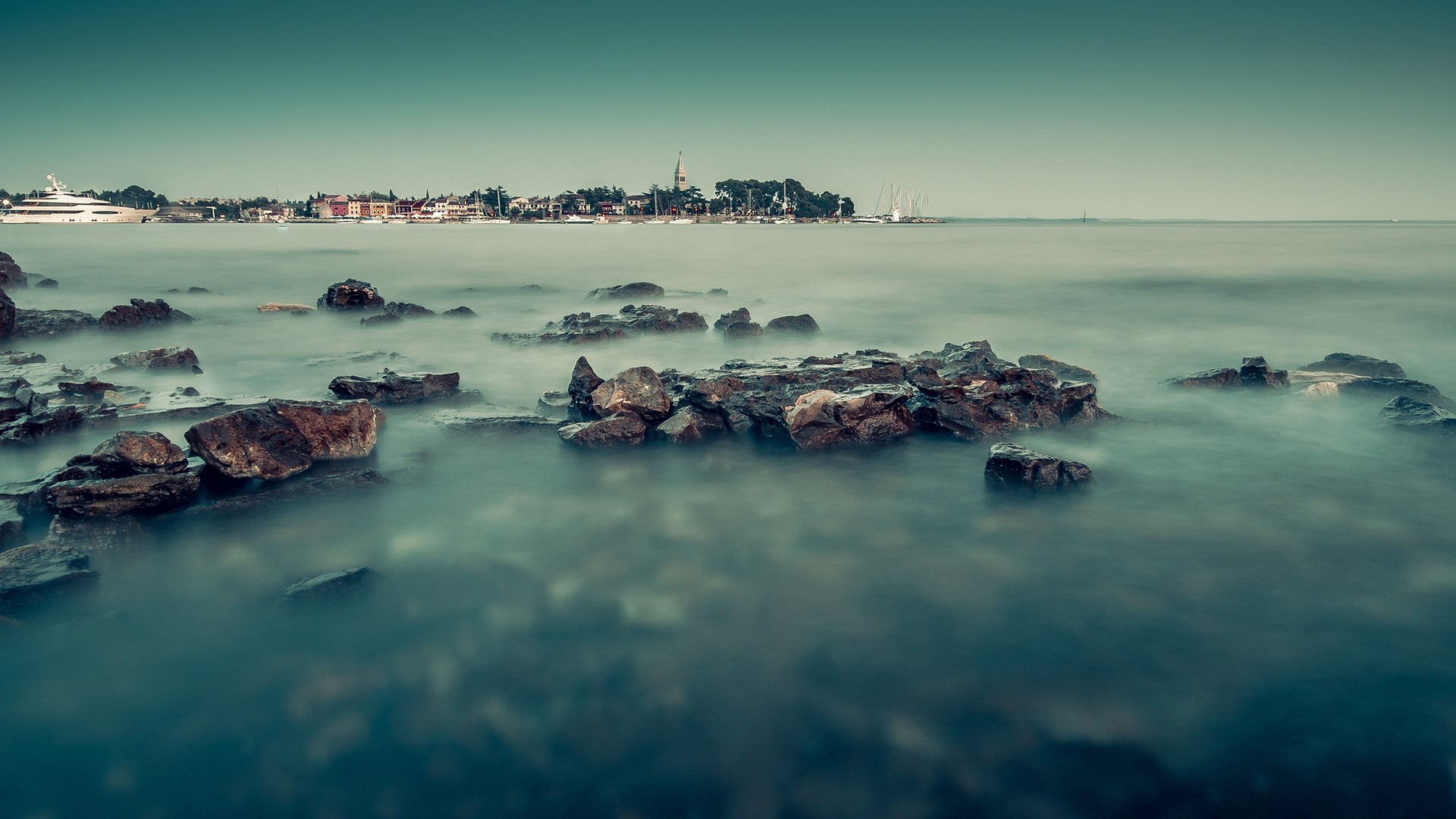 Rocky coastline with a distant town and yachts HD Wallpaper