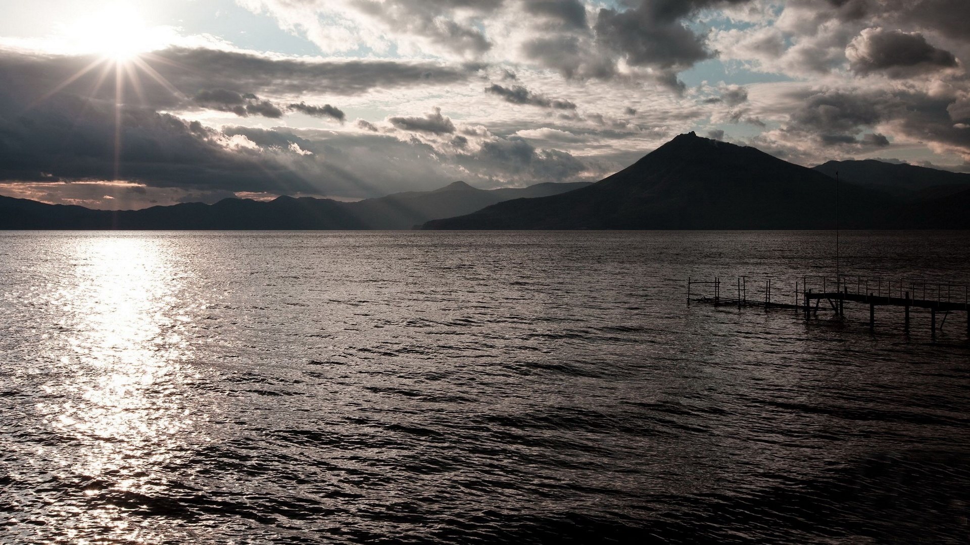 Sunset over a lake with mountains and a pier HD Wallpaper