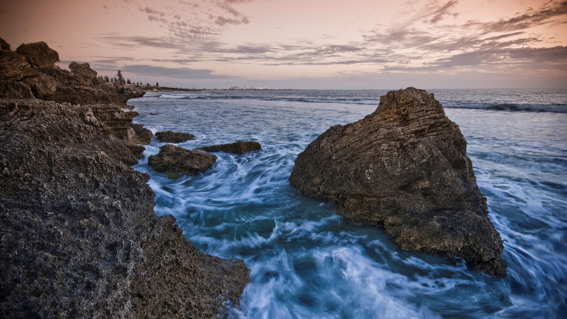 Rocky coastline with waves crashing at sunset HD Wallpaper