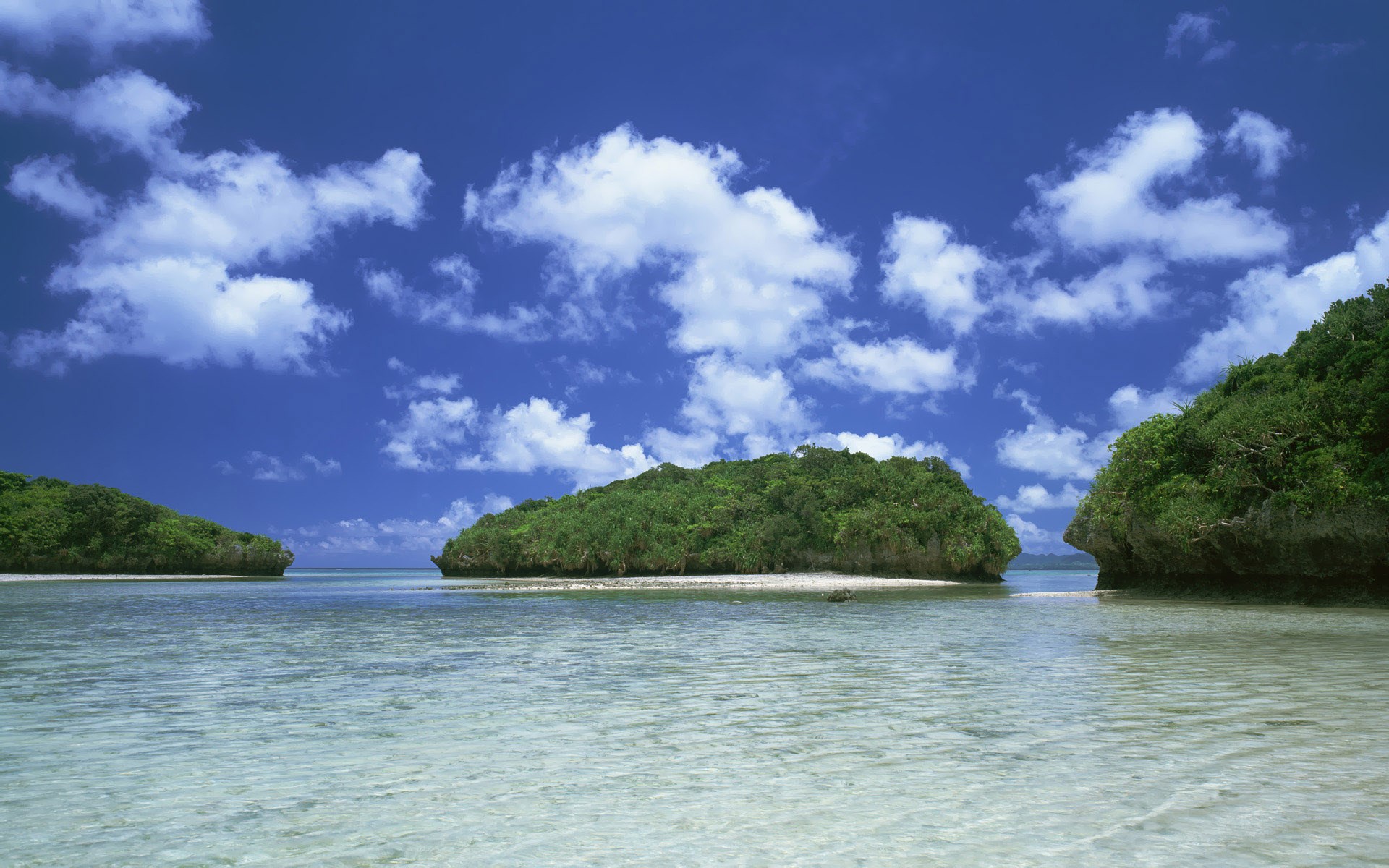 Islands in a clear blue ocean under a cloudy sky HD Wallpaper