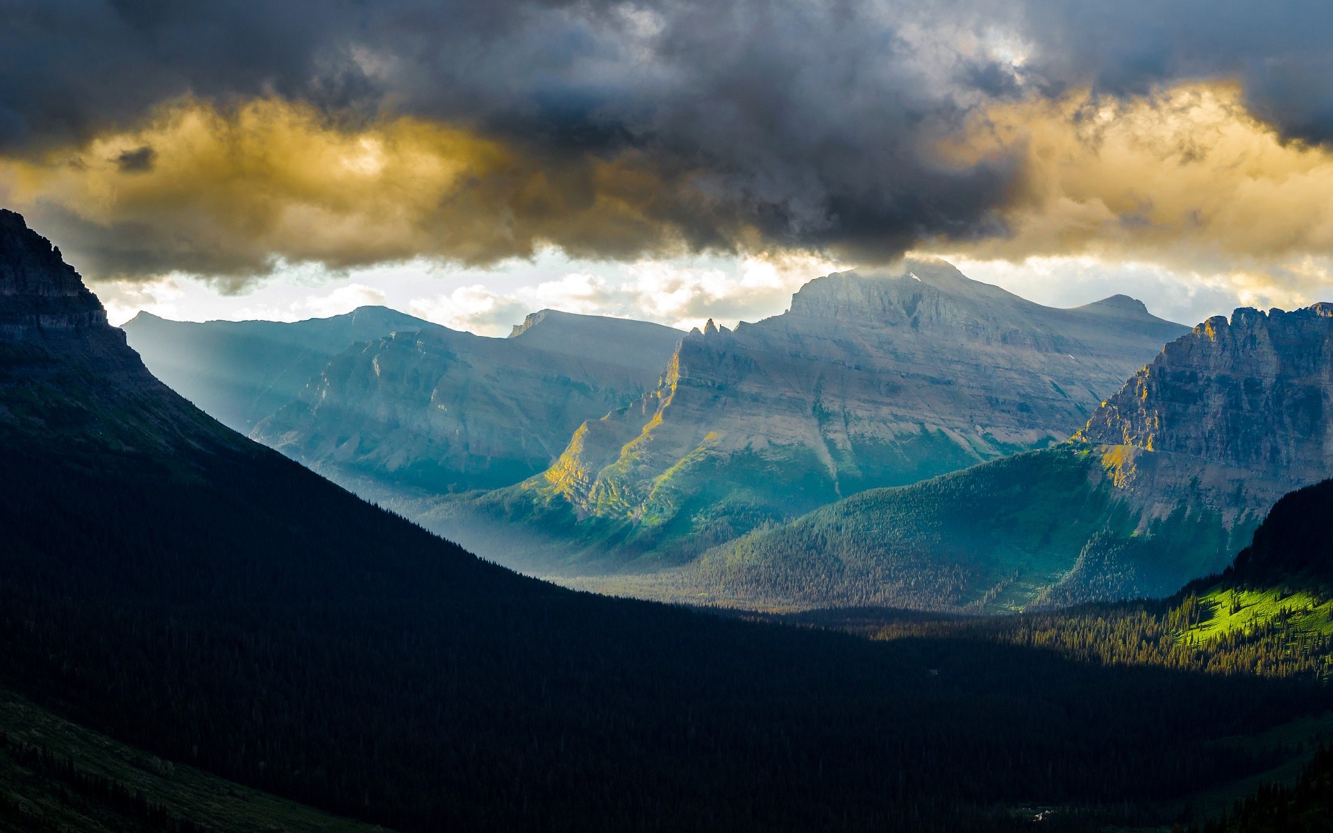 Sunlight beams through clouds onto mountains and forest HD Wallpaper