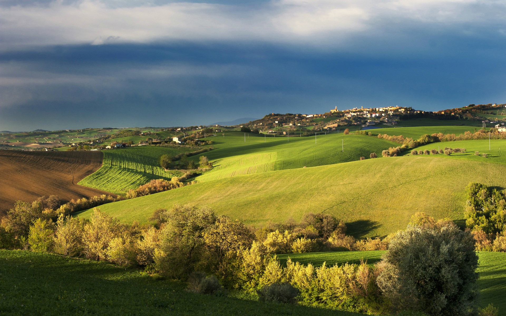 Rolling green hills with a town on the horizon HD Wallpaper
