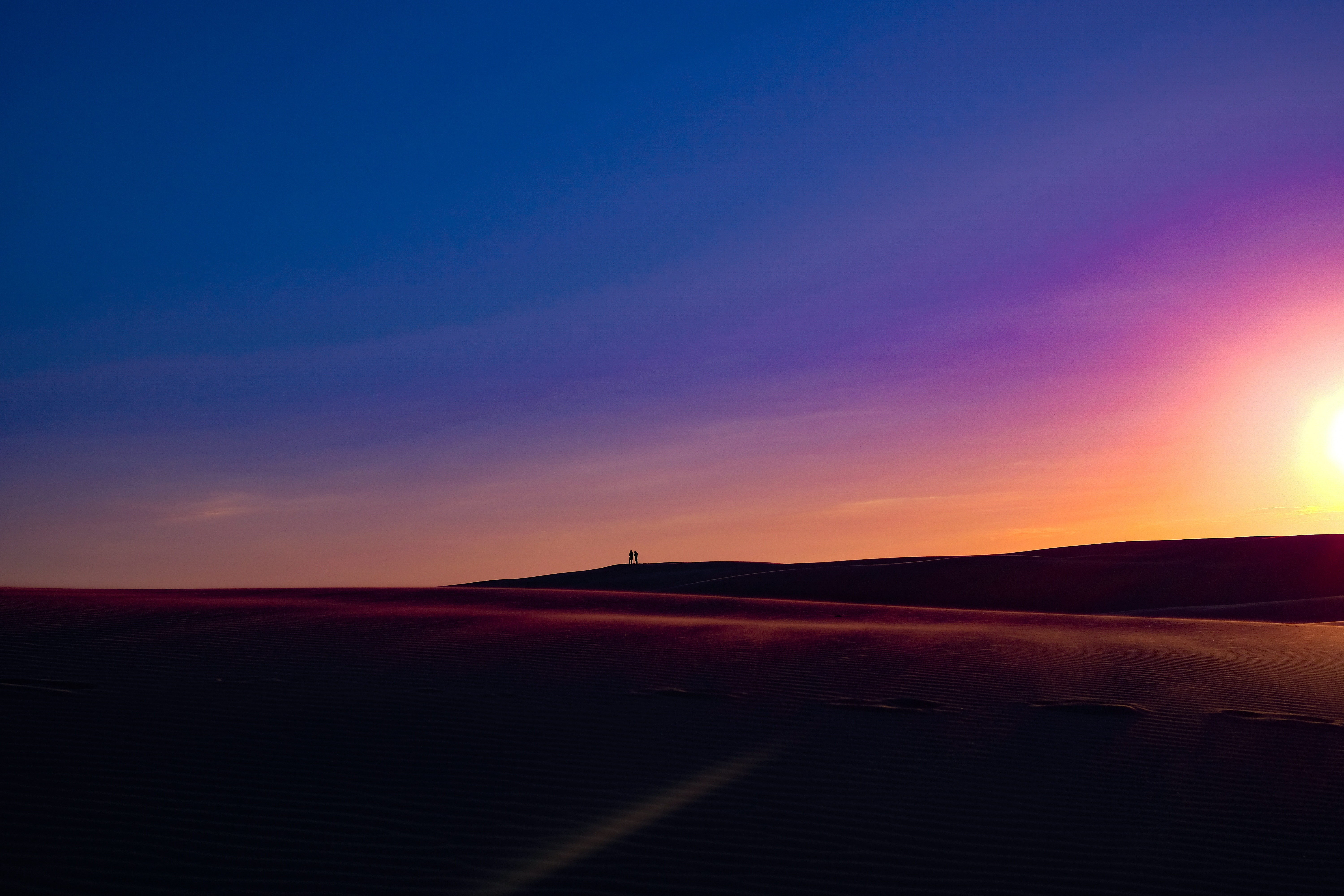 Two people silhouetted on a sand dune at sunset HD Wallpaper