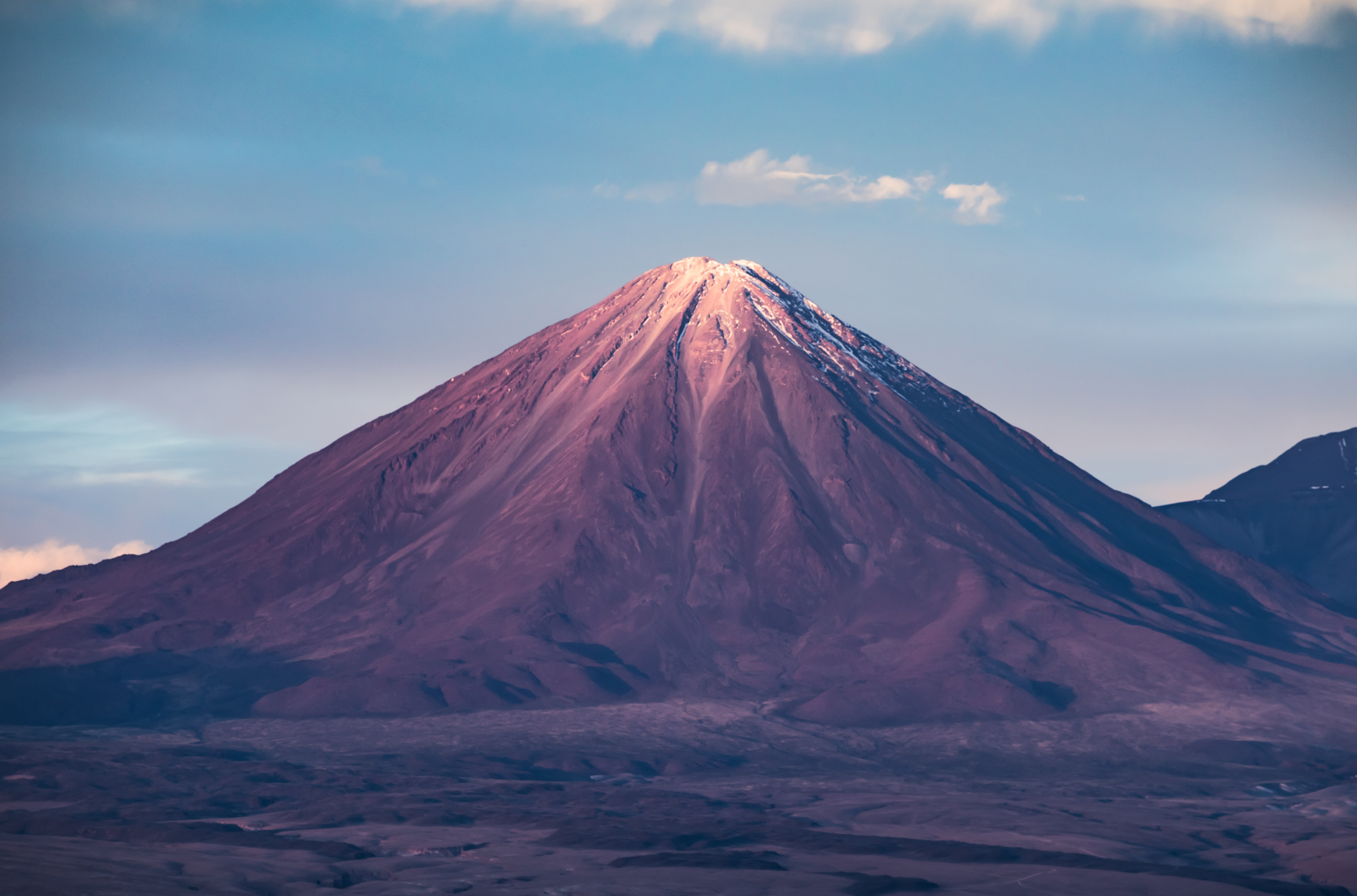 Volcano with snow-capped peak under a cloudy sky HD Wallpaper