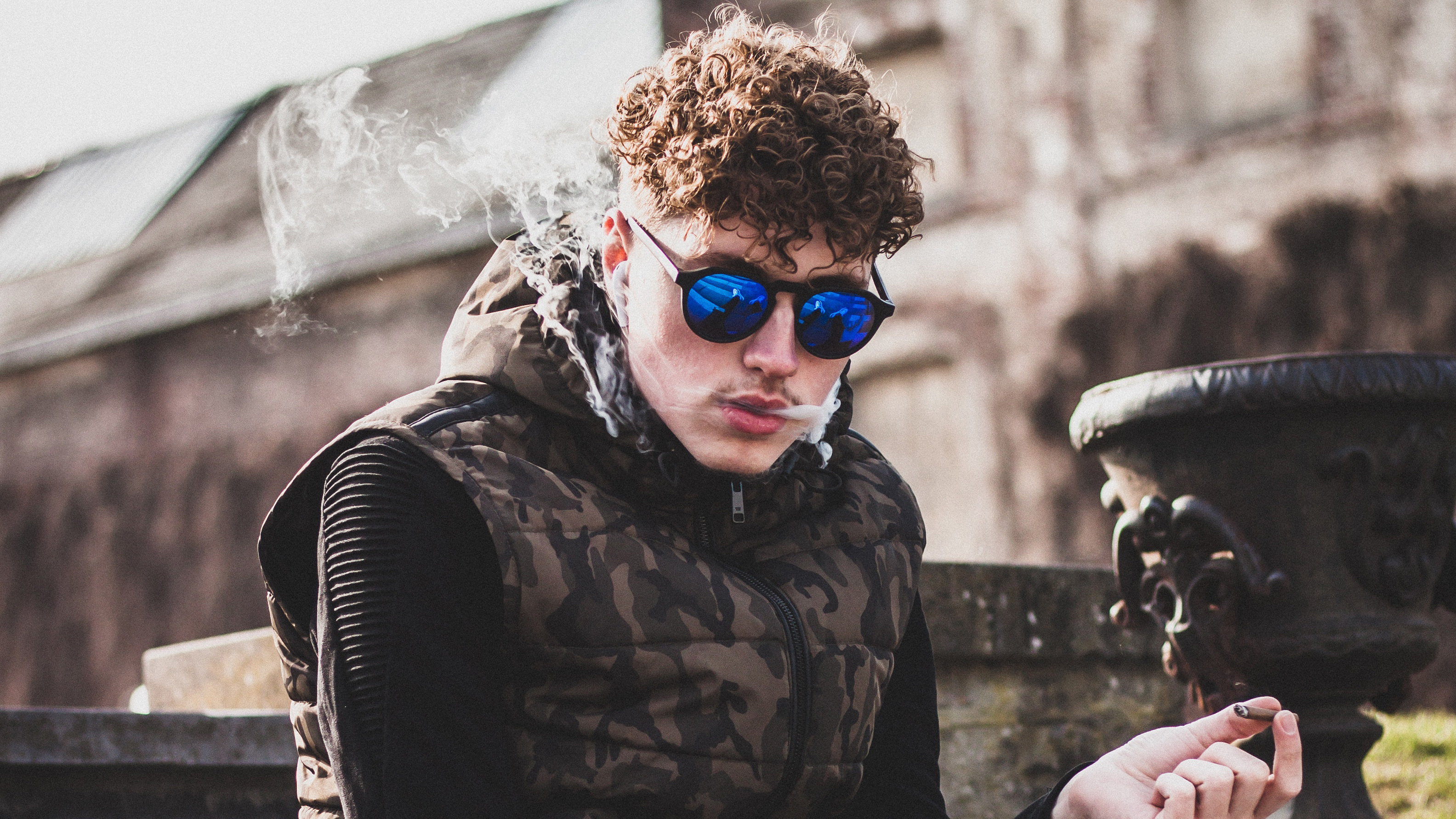 Man smoking with sunglasses and camouflage vest HD Wallpaper