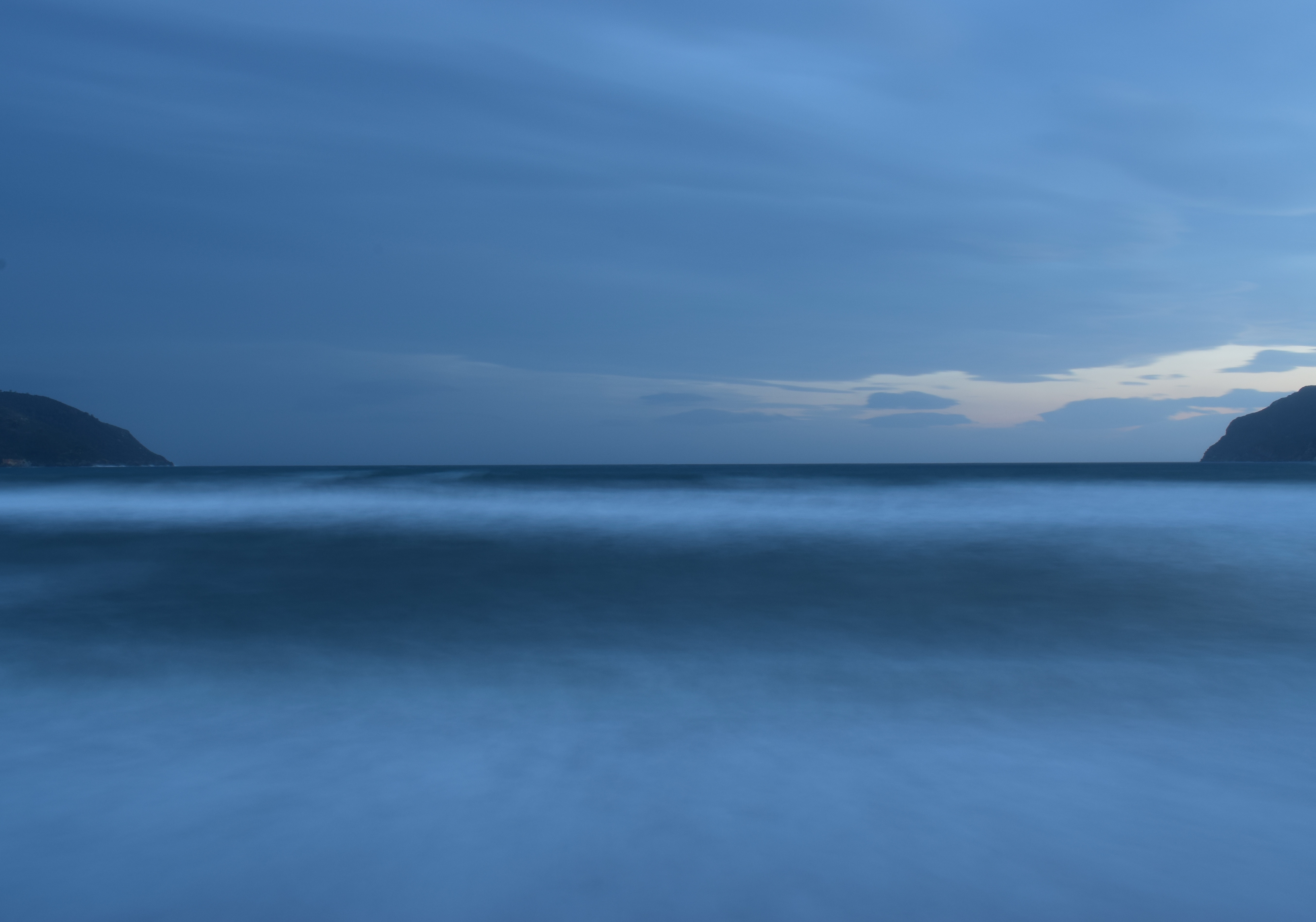 Ocean horizon at dusk with distant hills HD Wallpaper