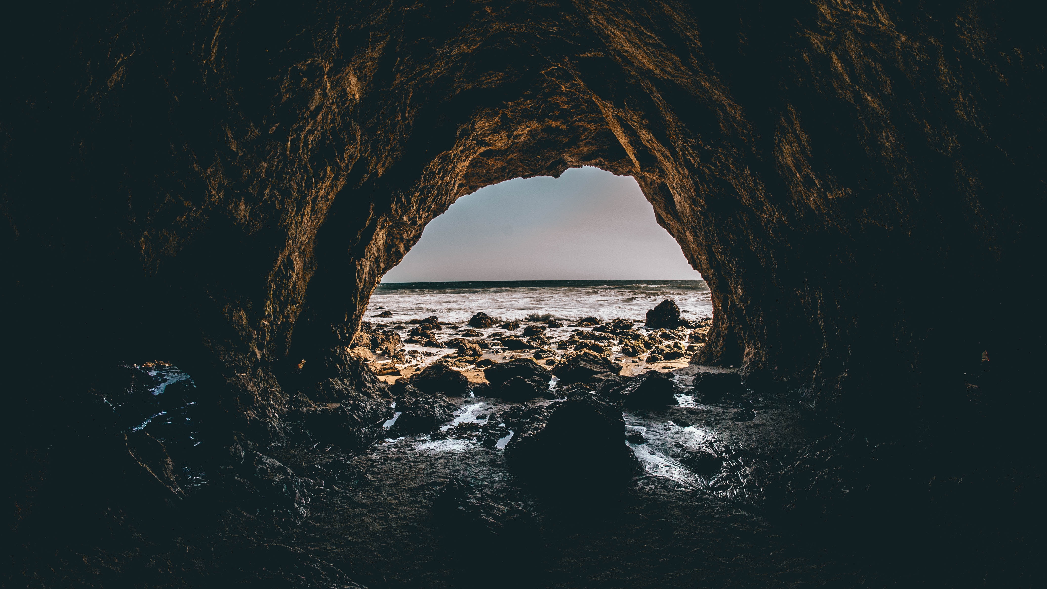 Cave entrance overlooking a rocky beach and ocean HD Wallpaper