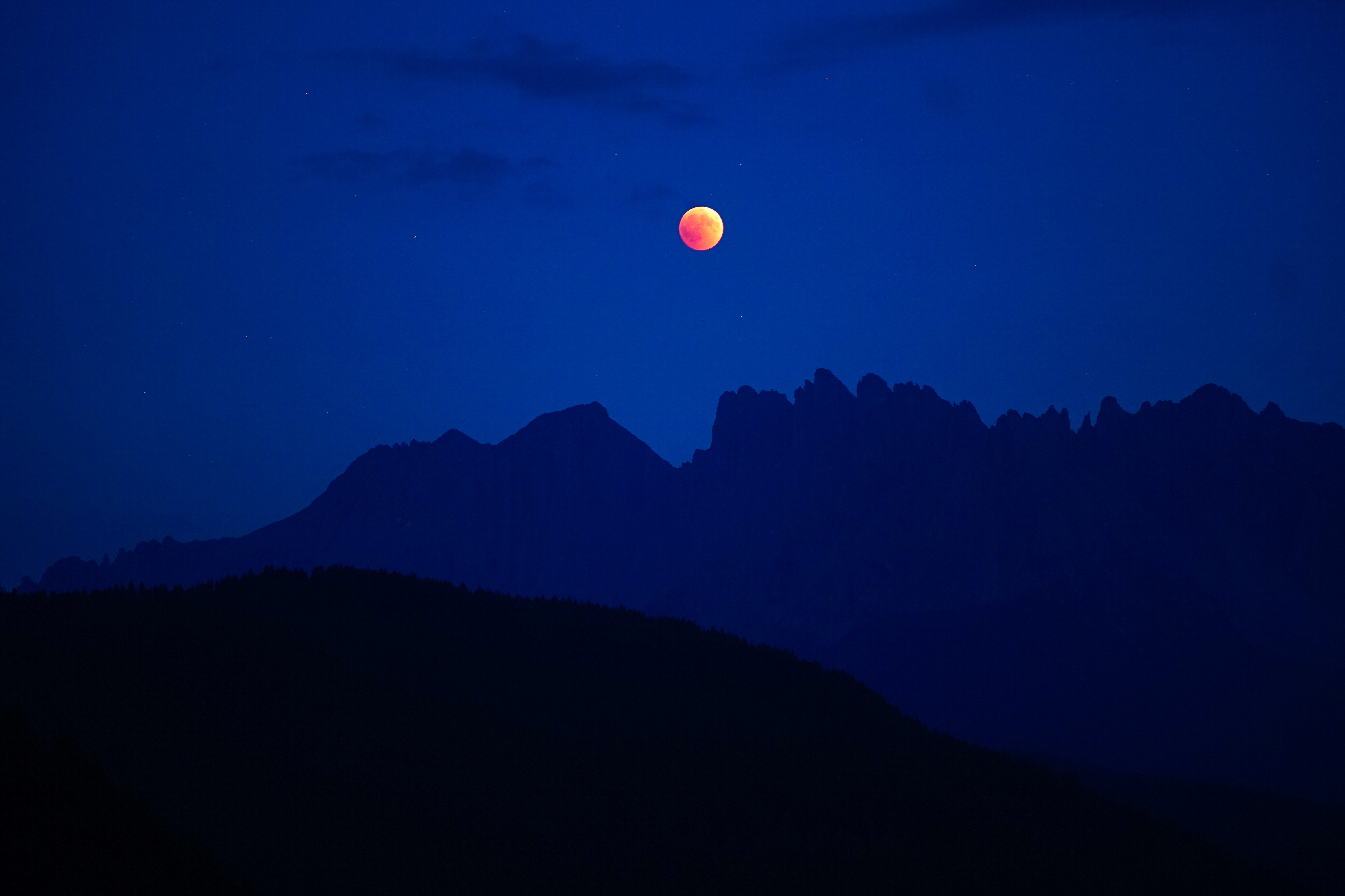Lunar eclipse over silhouetted mountains at night HD Wallpaper