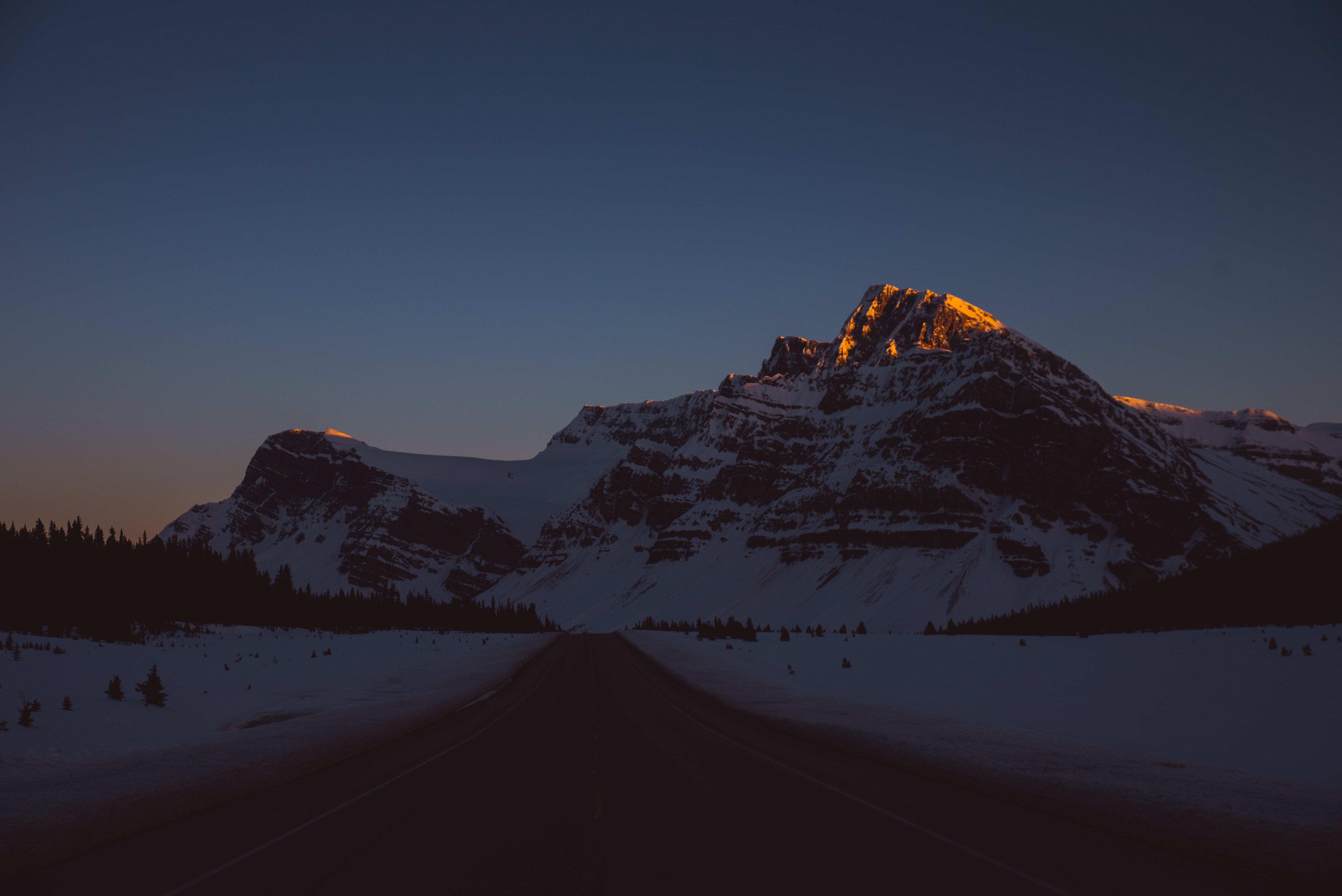 Snowy mountains at sunset with a road HD Wallpaper