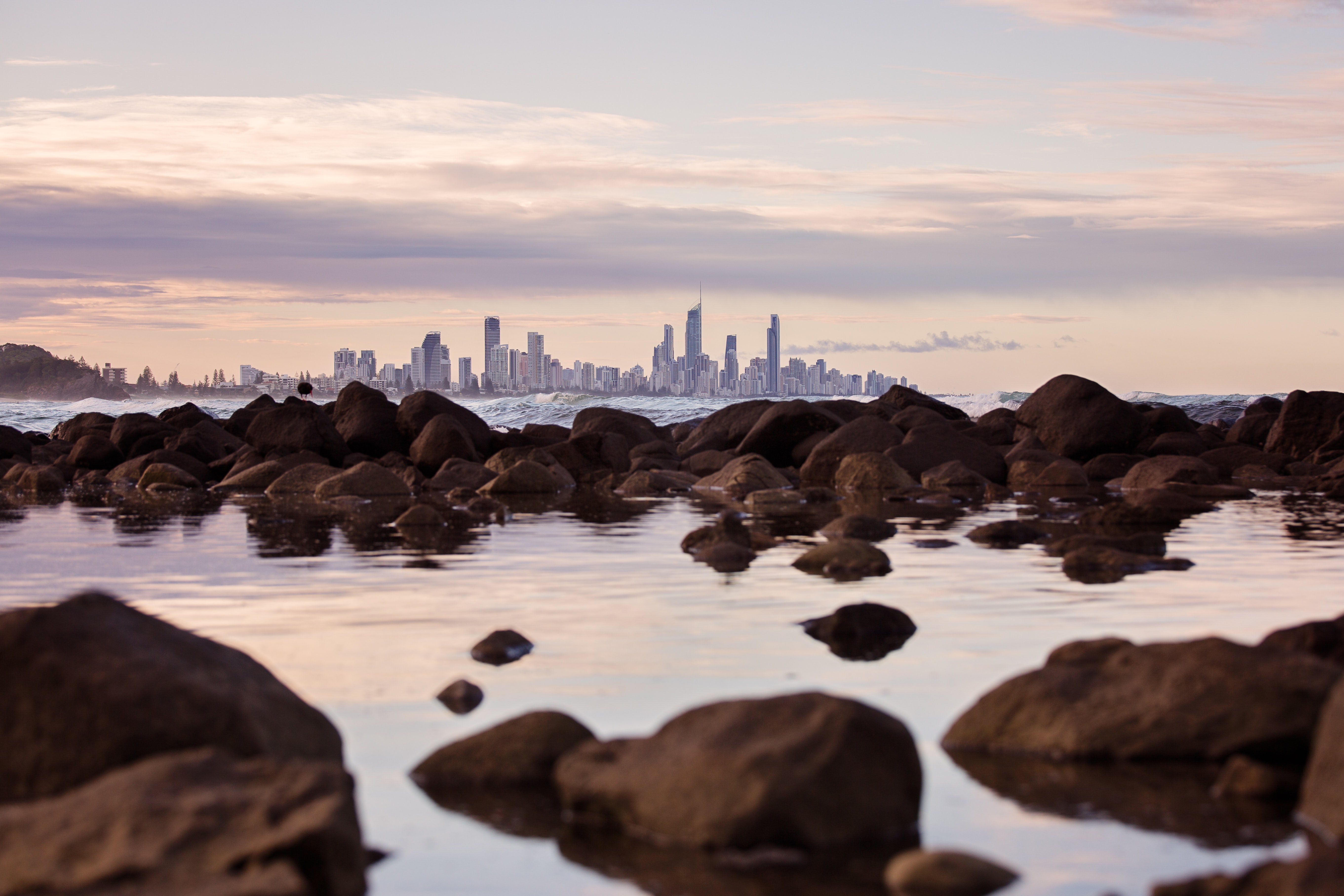 City skyline over rocks and ocean at sunset HD Wallpaper