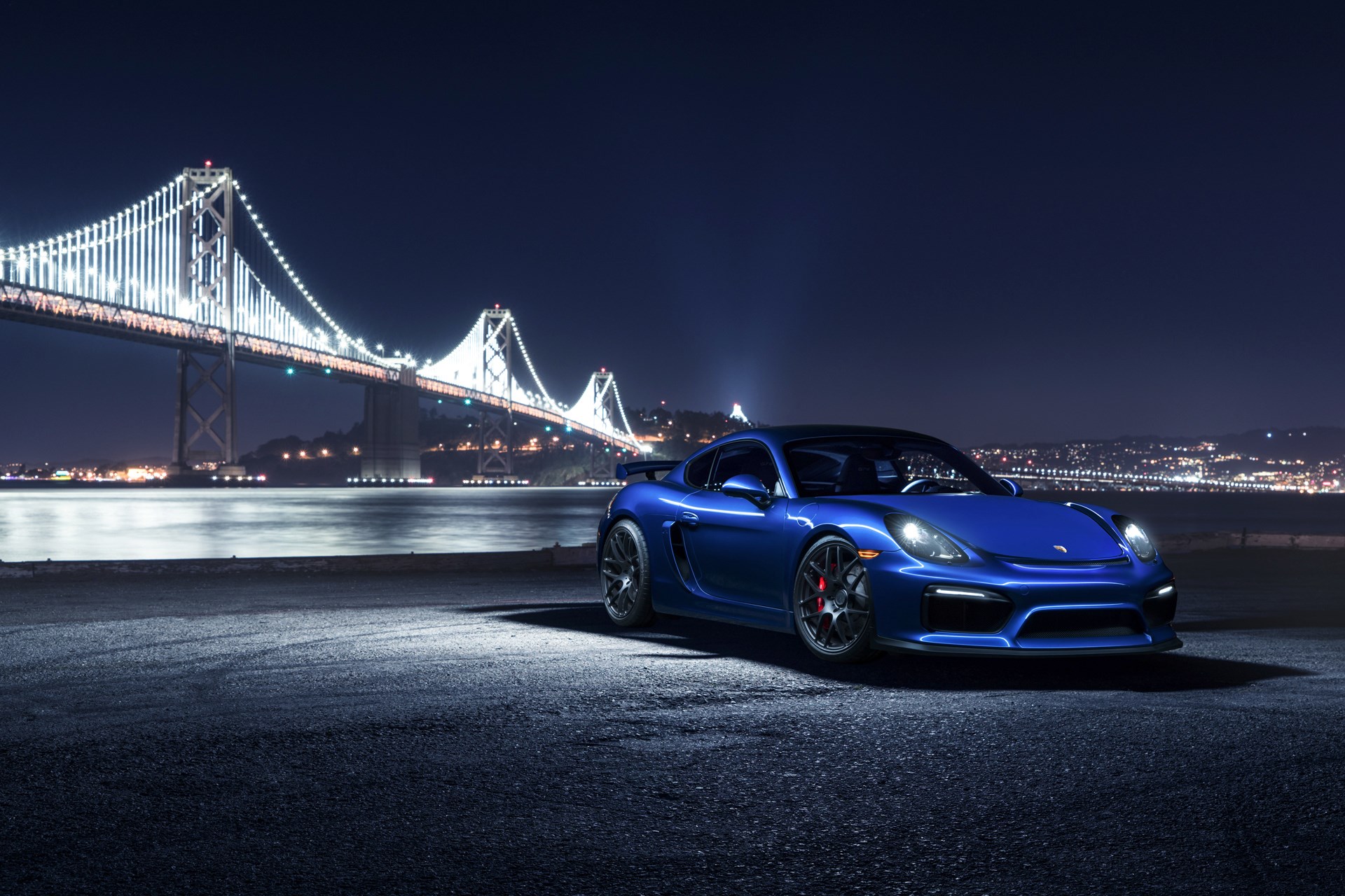 Blue Porsche Cayman GT4 parked at night with bridge in background HD Wallpaper