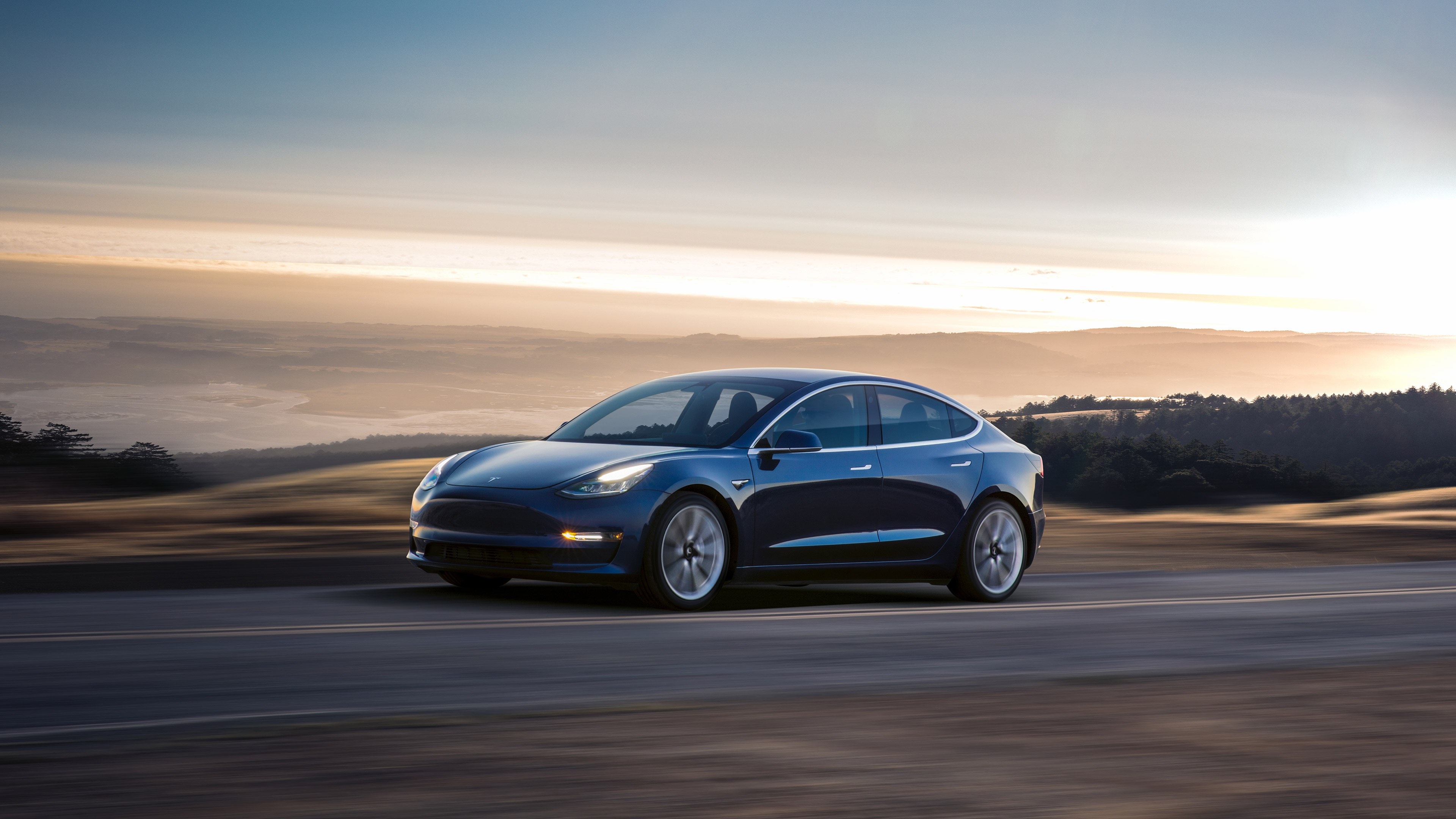 Tesla Model 3 driving on a road at sunset HD Wallpaper