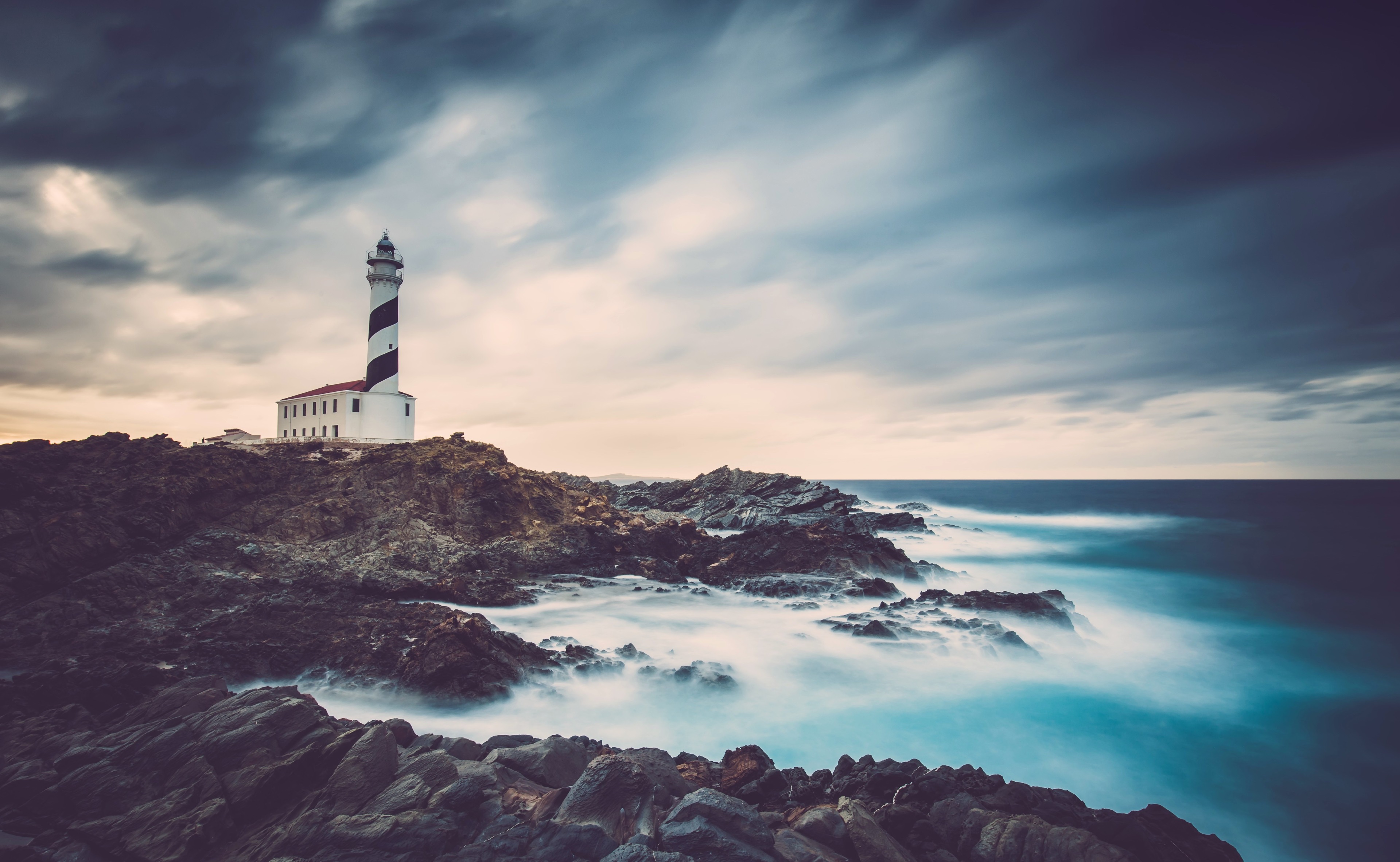 Lighthouse on rocky coast with stormy sky HD Wallpaper