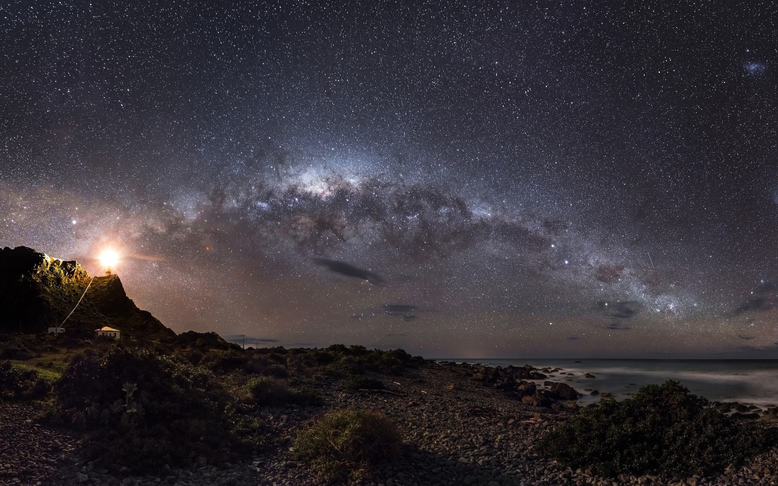 Milky Way over a rocky coastline with a lighthouse HD Wallpaper