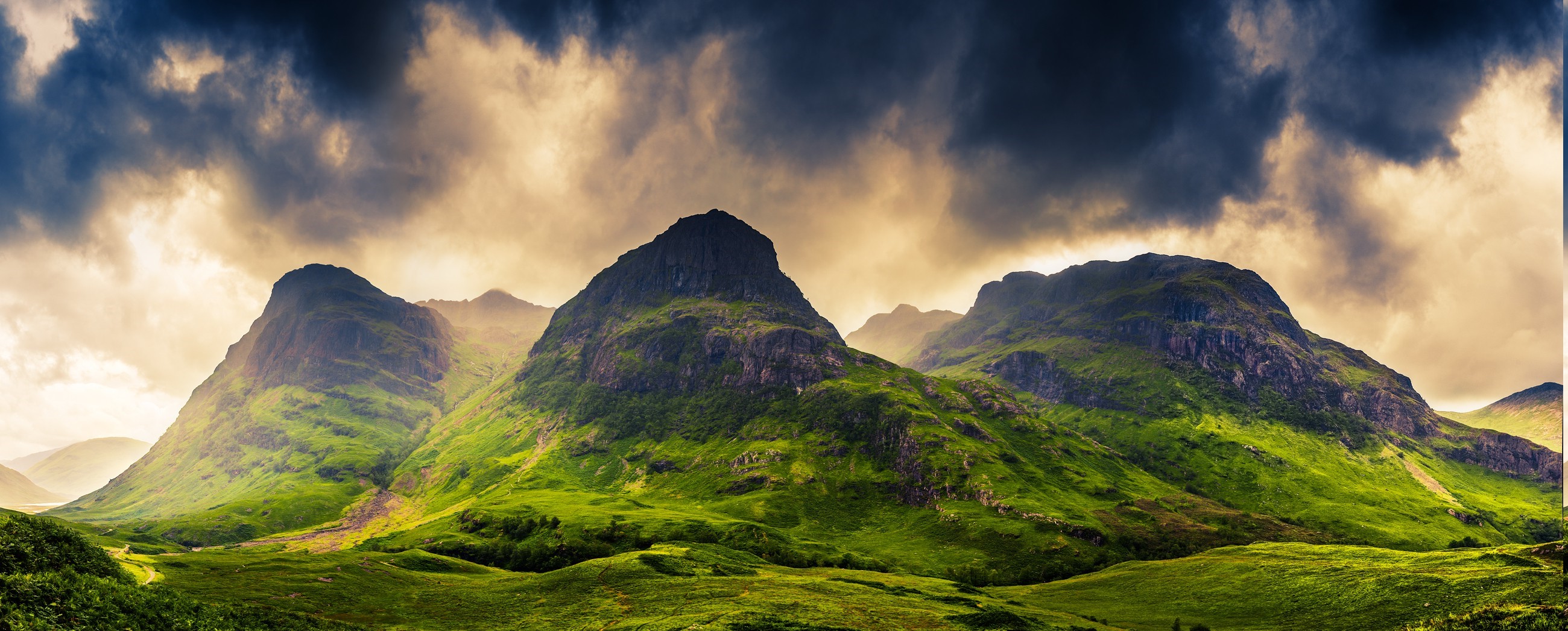 Three Sisters mountains in Glencoe, Scotland under dramatic clouds HD Wallpaper